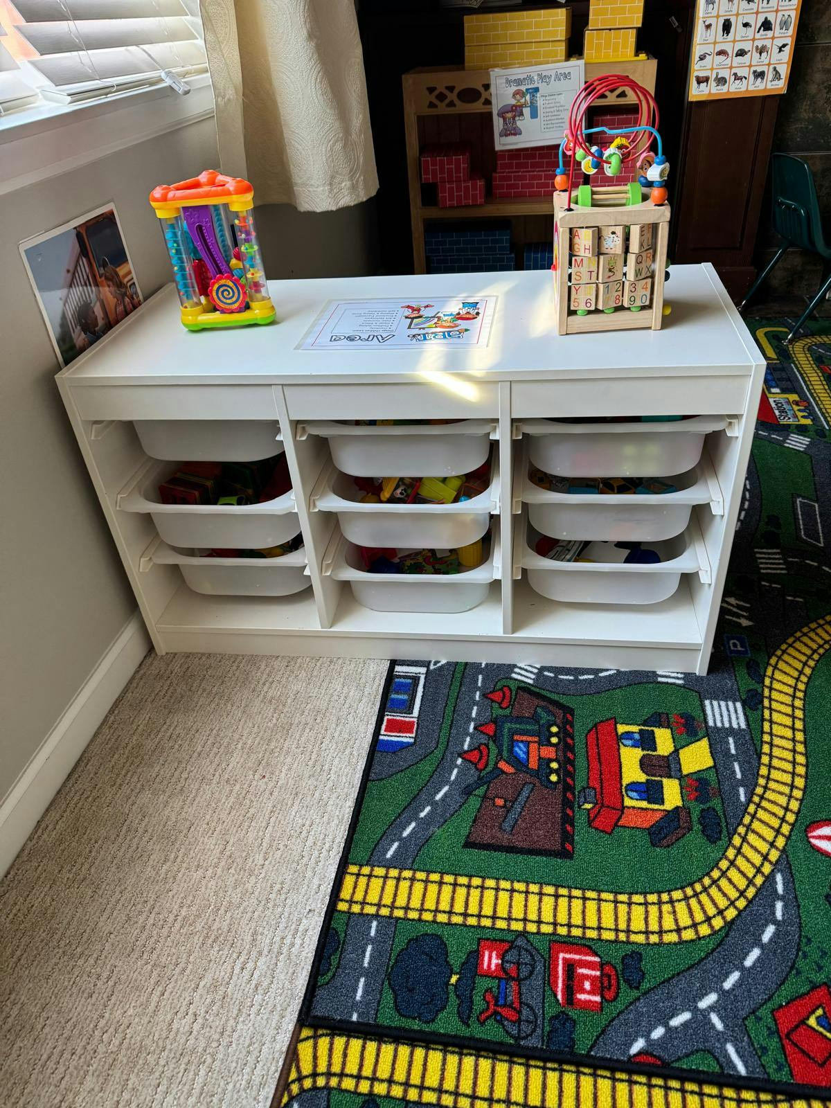 White storage unit with bins and toys on top, next to a play rug