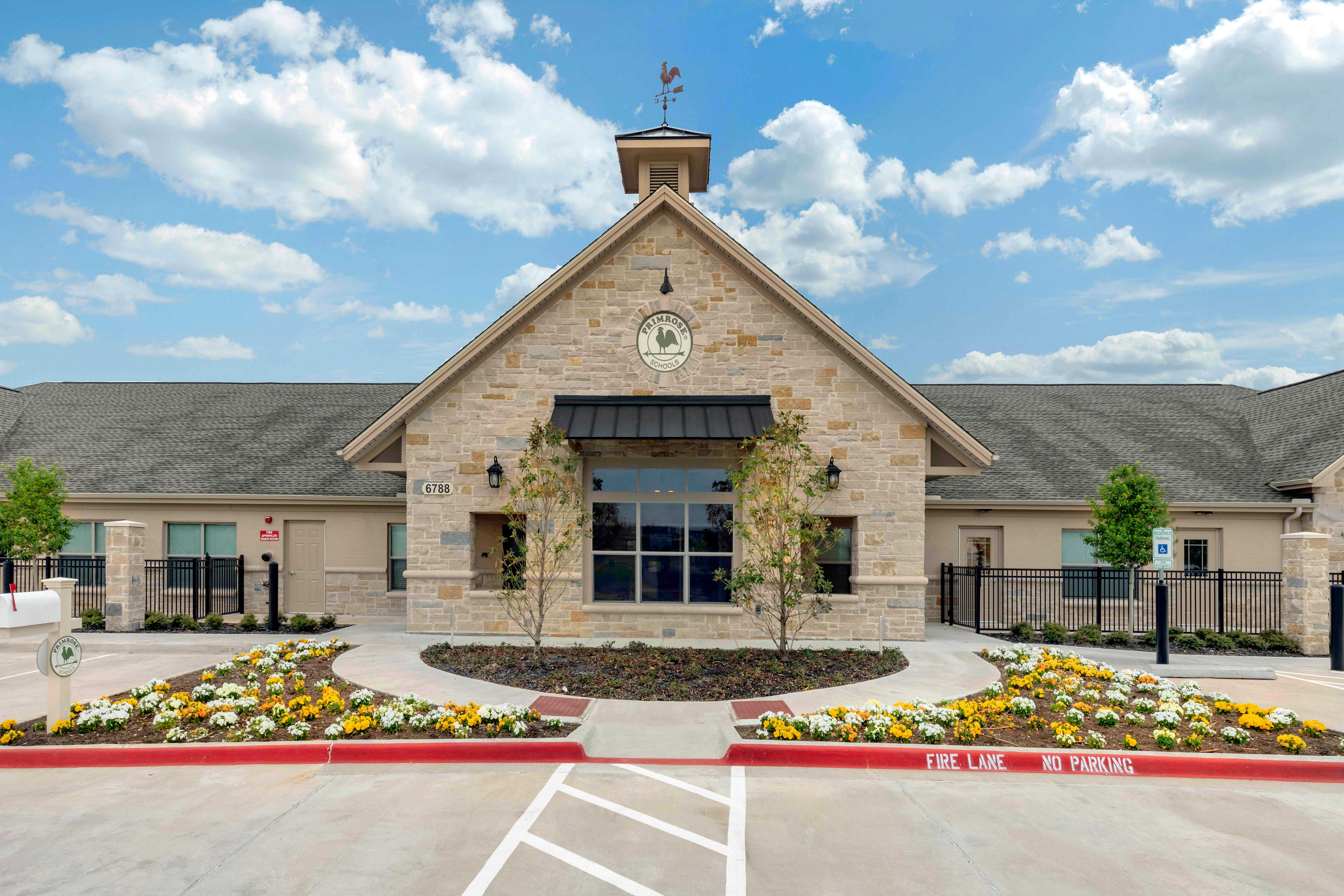 Stone building with a weather vane on top, Primrose Schools sign, flowerbeds in front