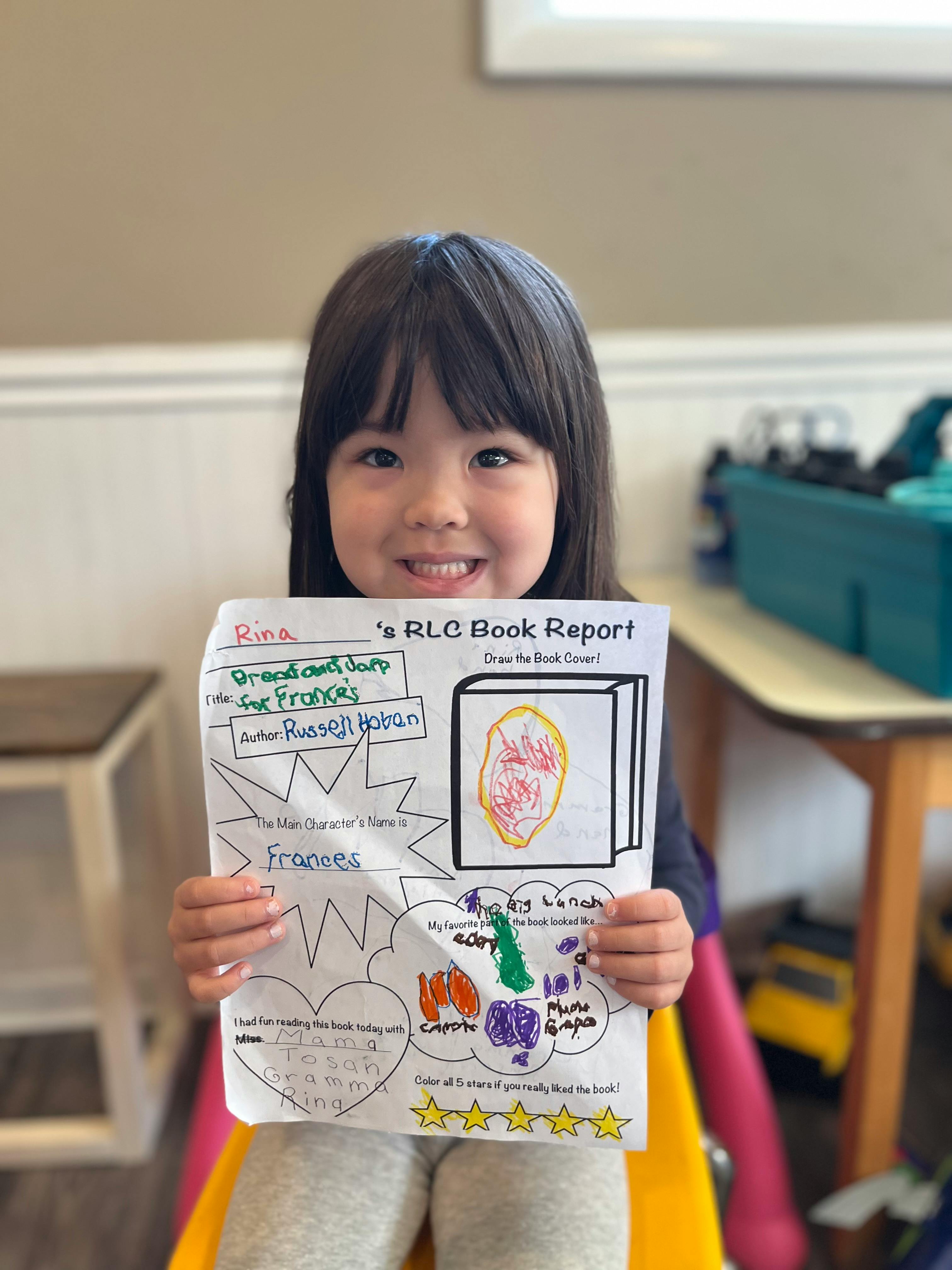 Child holding up a book report with drawings and text