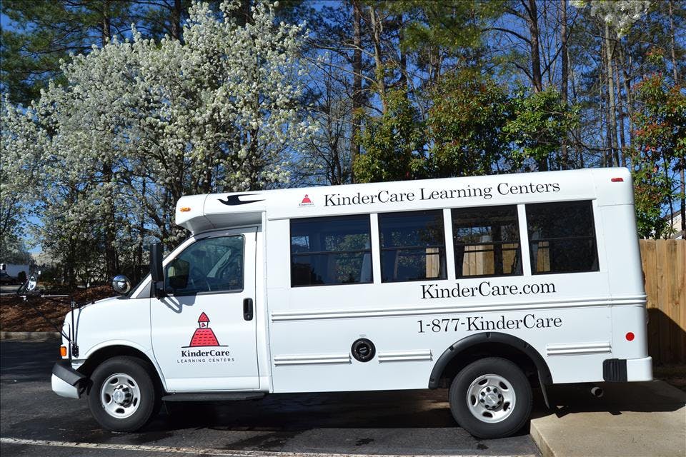 White KinderCare bus parked on a paved lot with trees in the background