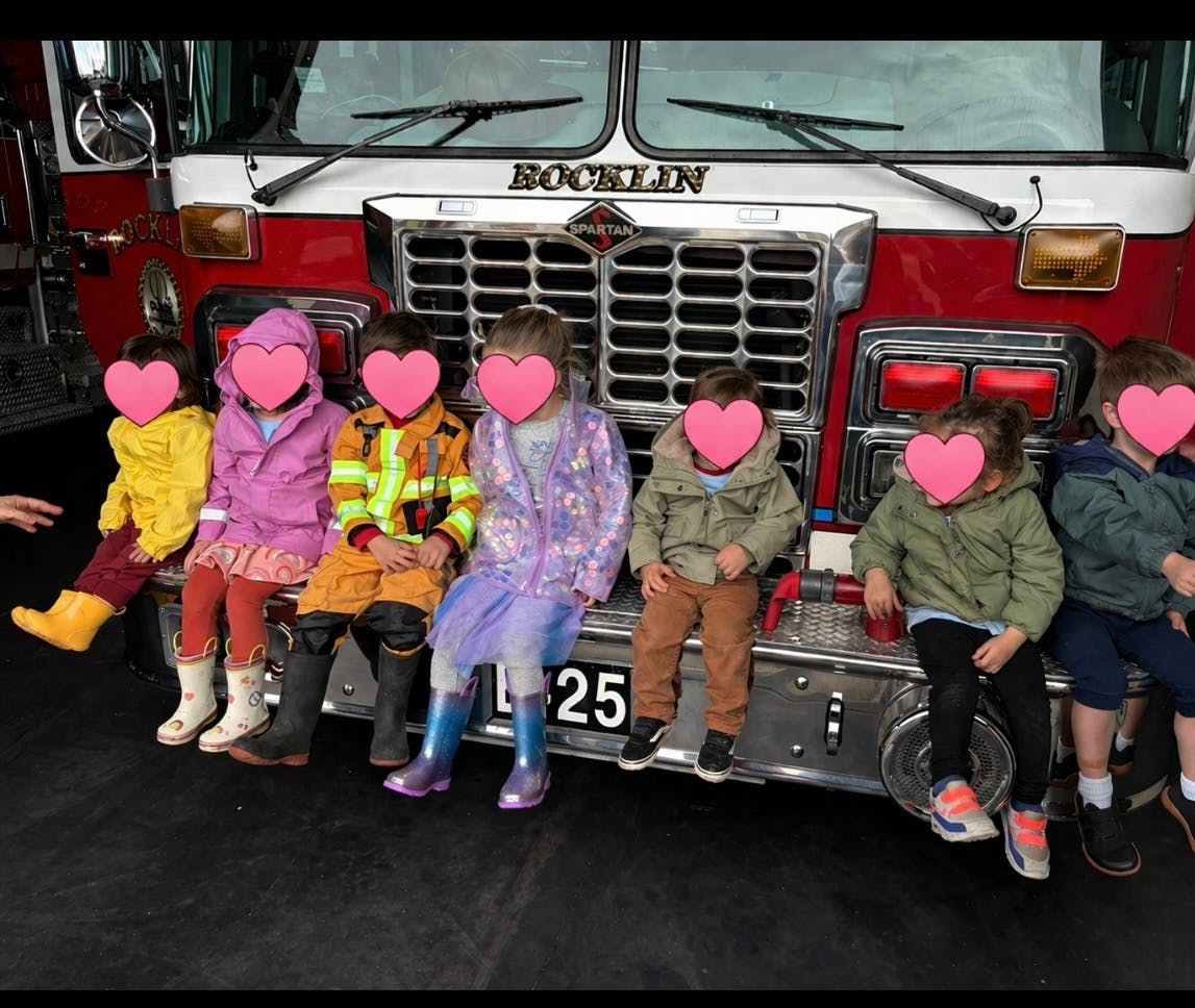 Group of children sitting on the front bumper of a fire truck