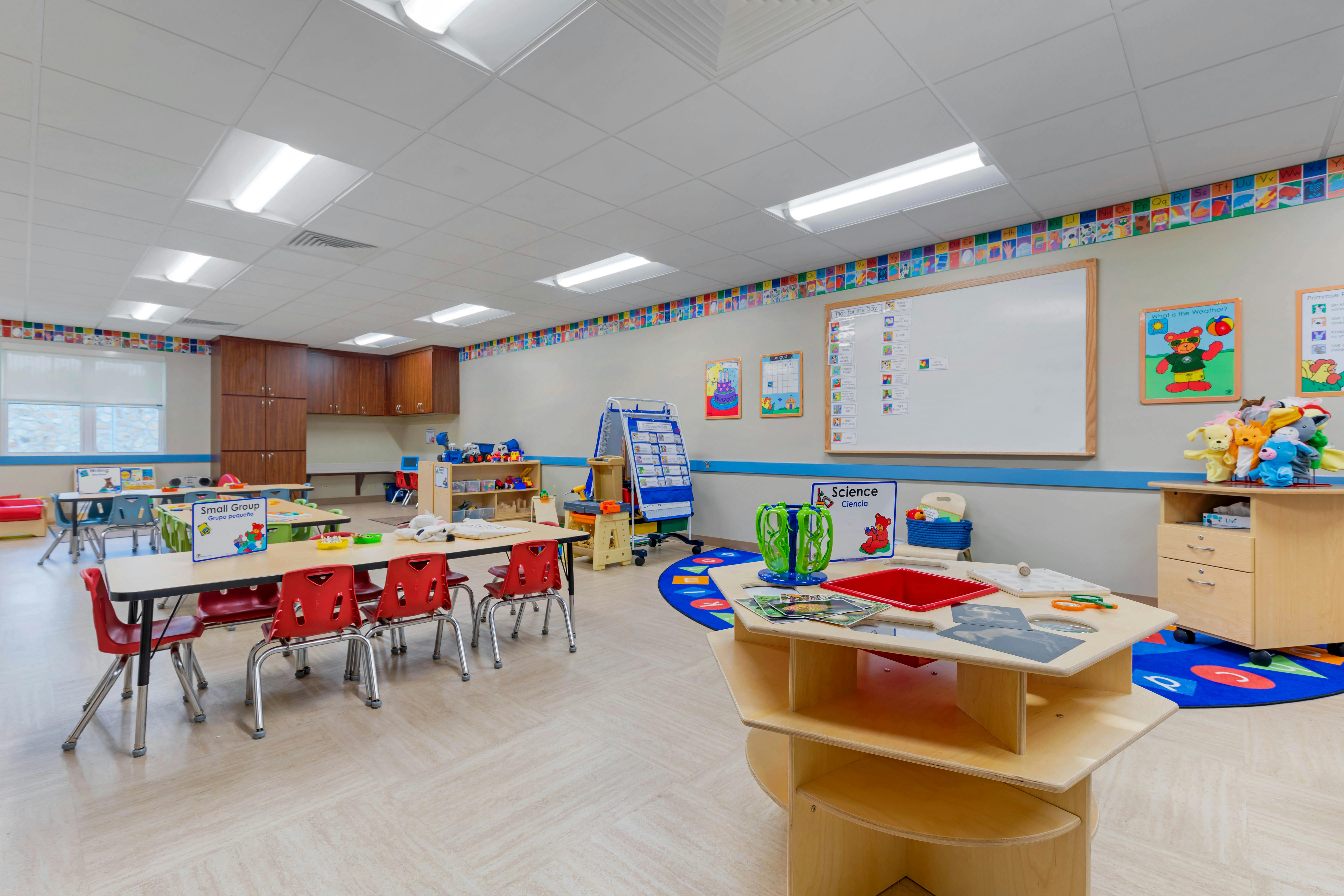 Classroom with small tables and chairs, a whiteboard, and activity stations