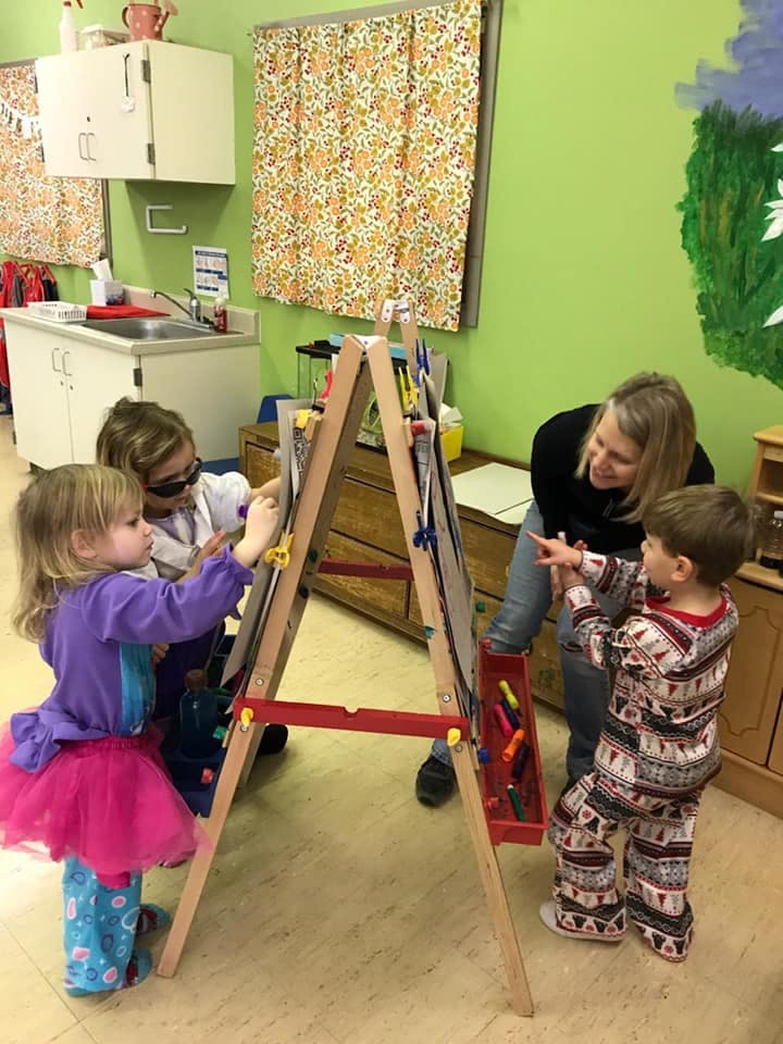 Two children and two adults drawing on an easel