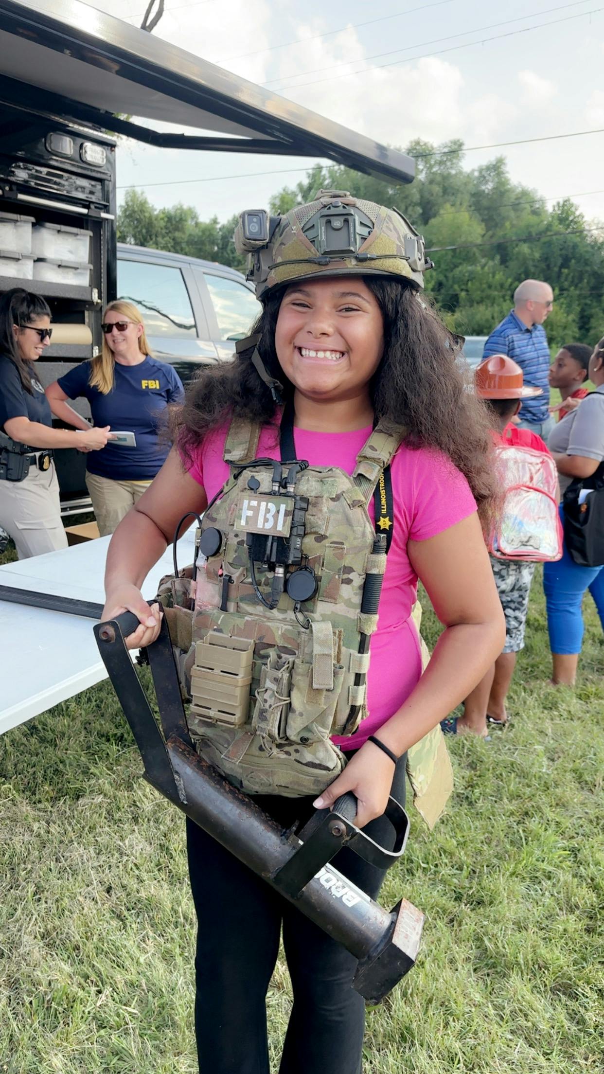 Child wearing a tactical vest and helmet, holding an object