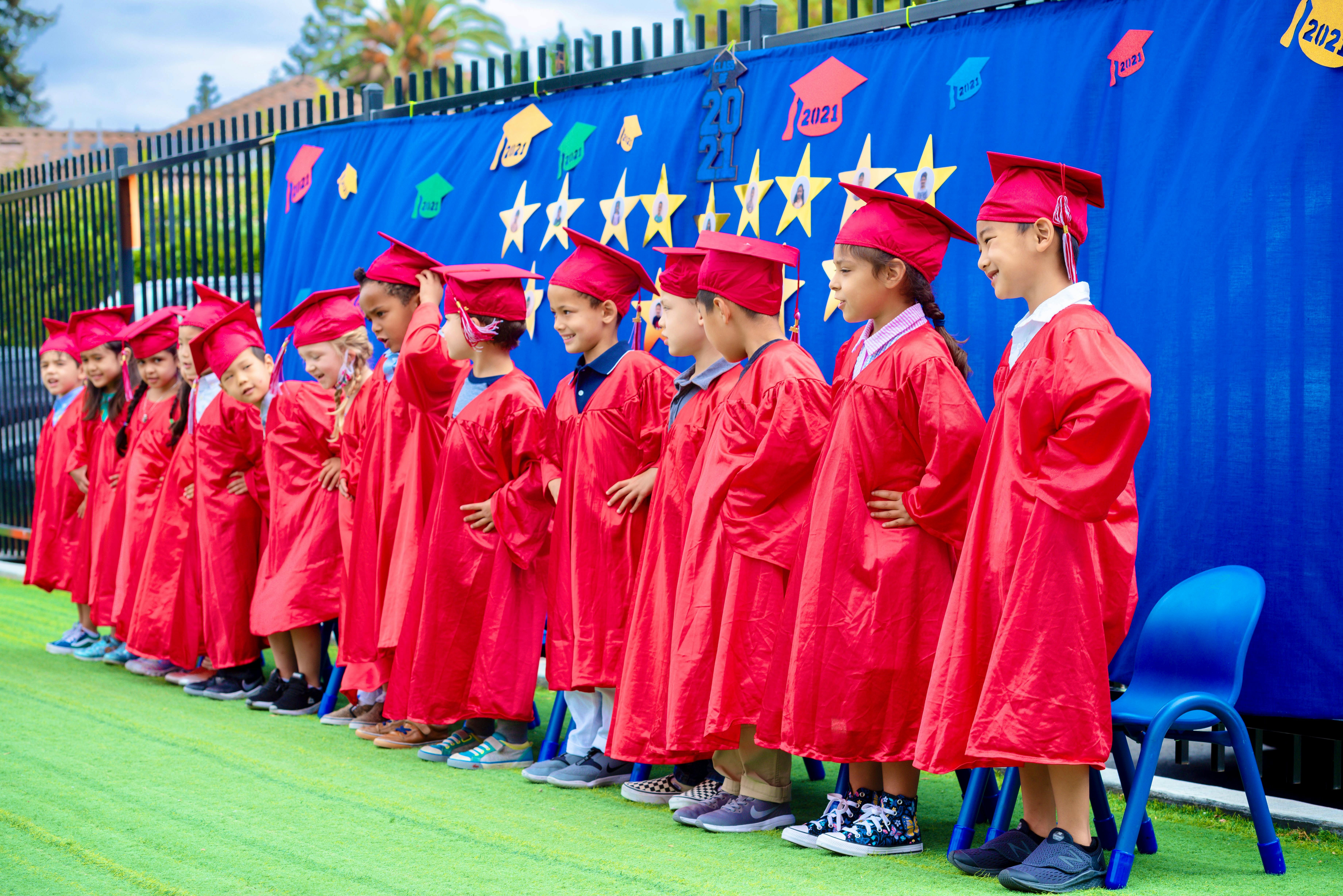 Children in red graduation caps and gowns standing in a line