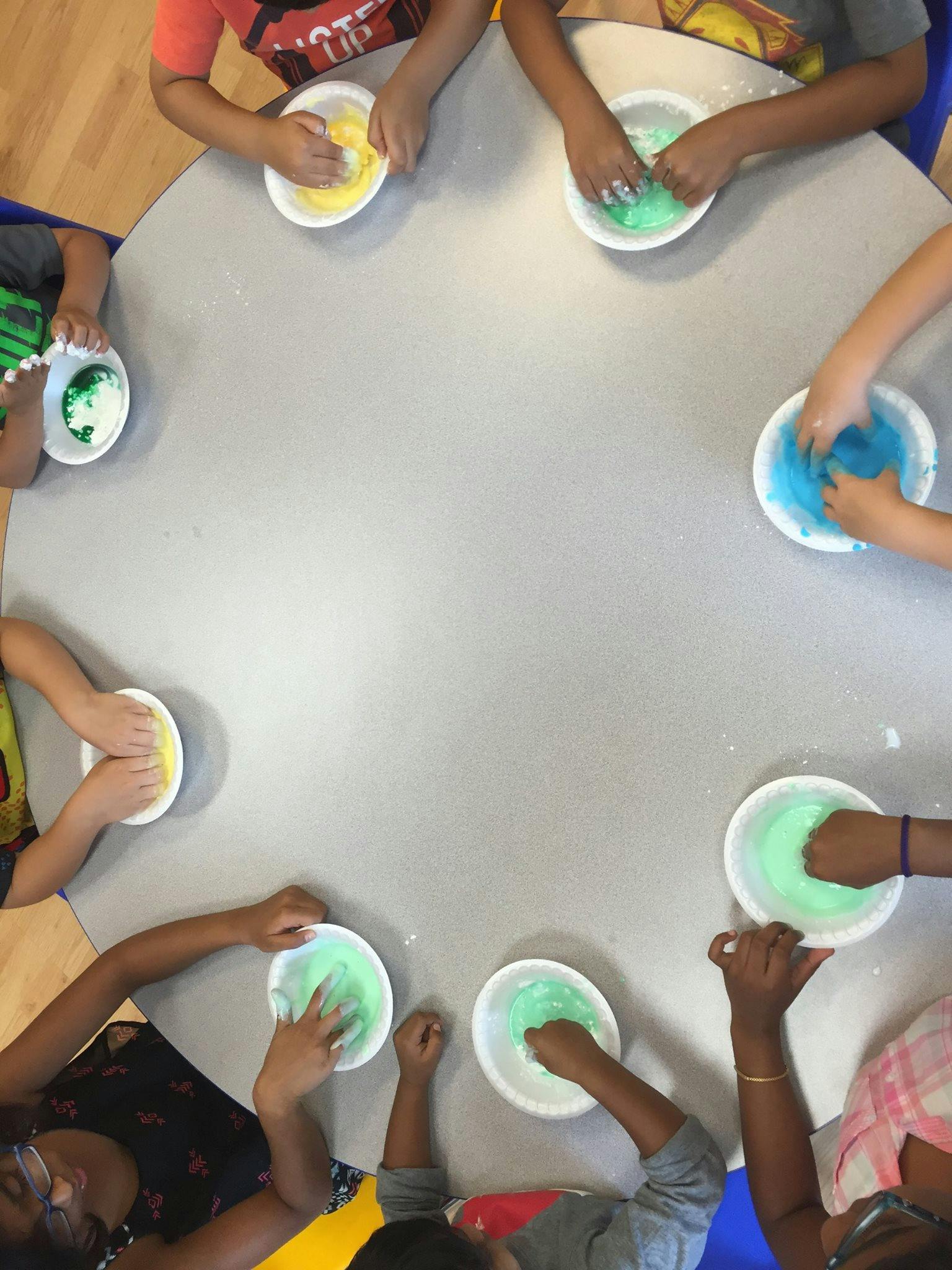 Children's hands mixing colorful slime in bowls on a table