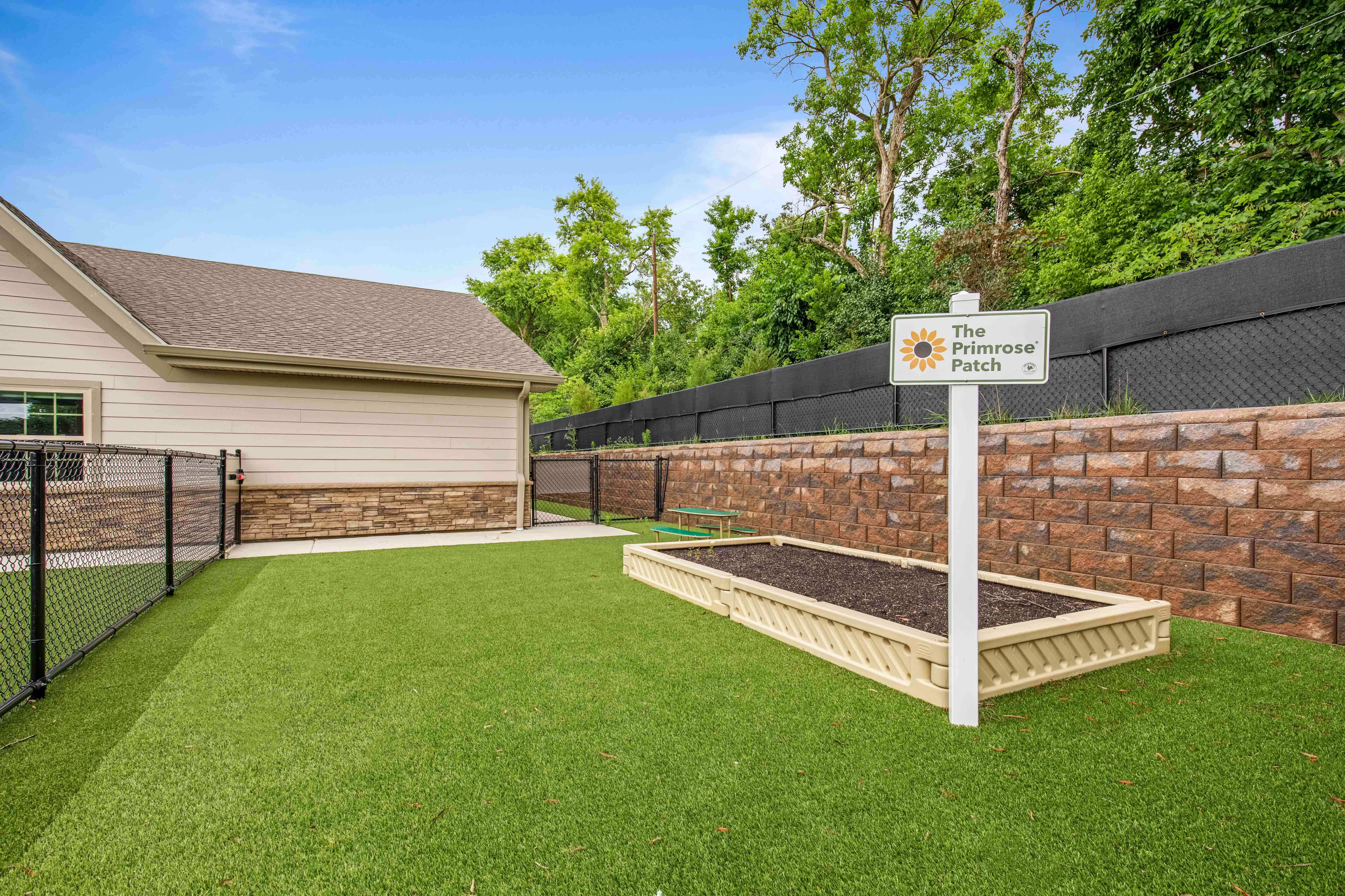 Sign for "The Primrose Patch" next to a planter box on artificial turf