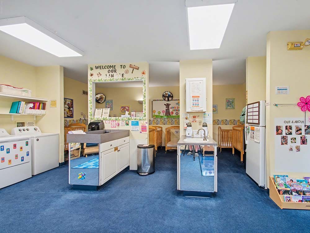 A childcare room with cribs, changing stations, a sink, and laundry machines