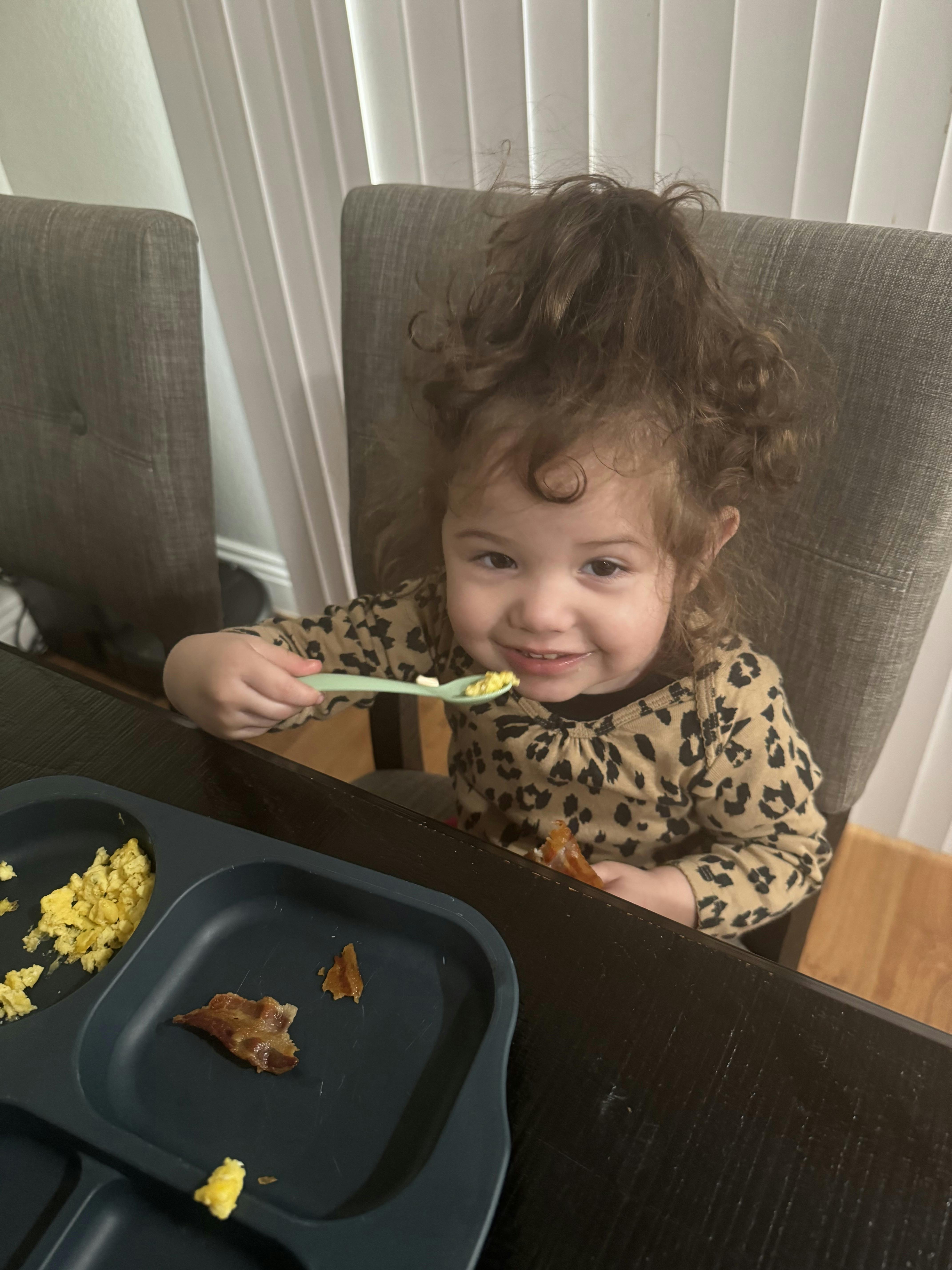 Child in leopard print shirt eating scrambled eggs with a spoon