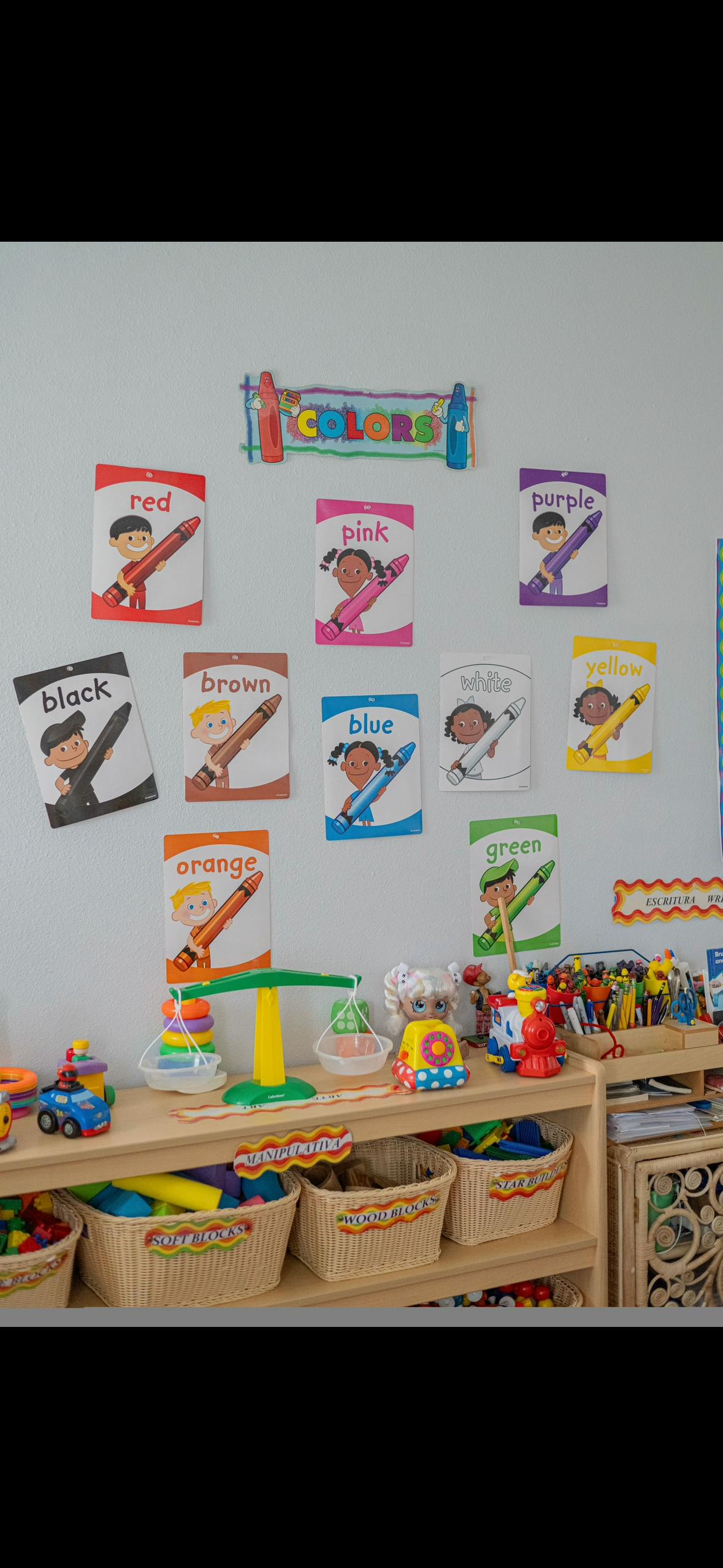 Classroom wall with color charts and a shelf with toys and baskets