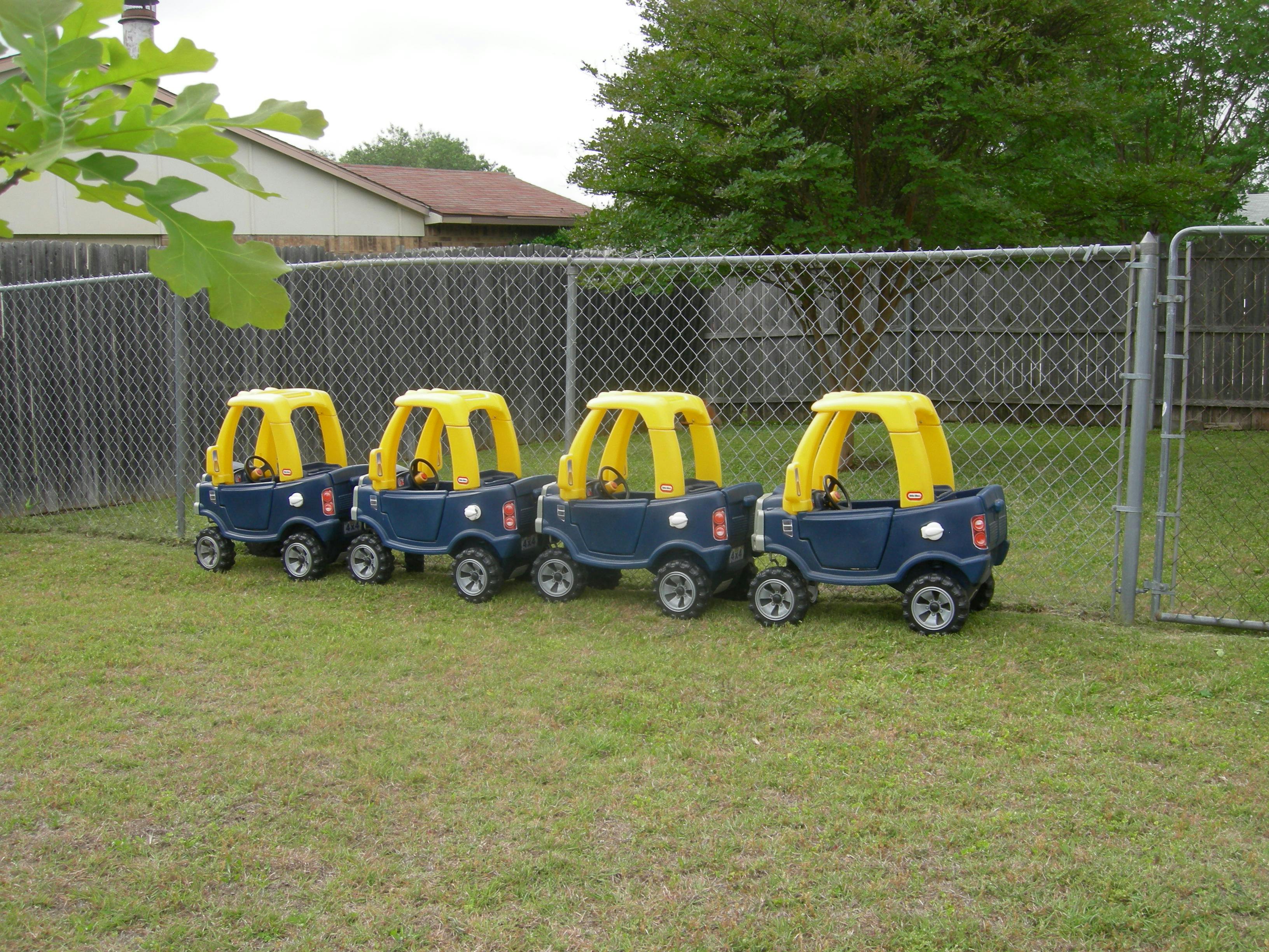 Four toy cars lined up on grass next to a fence