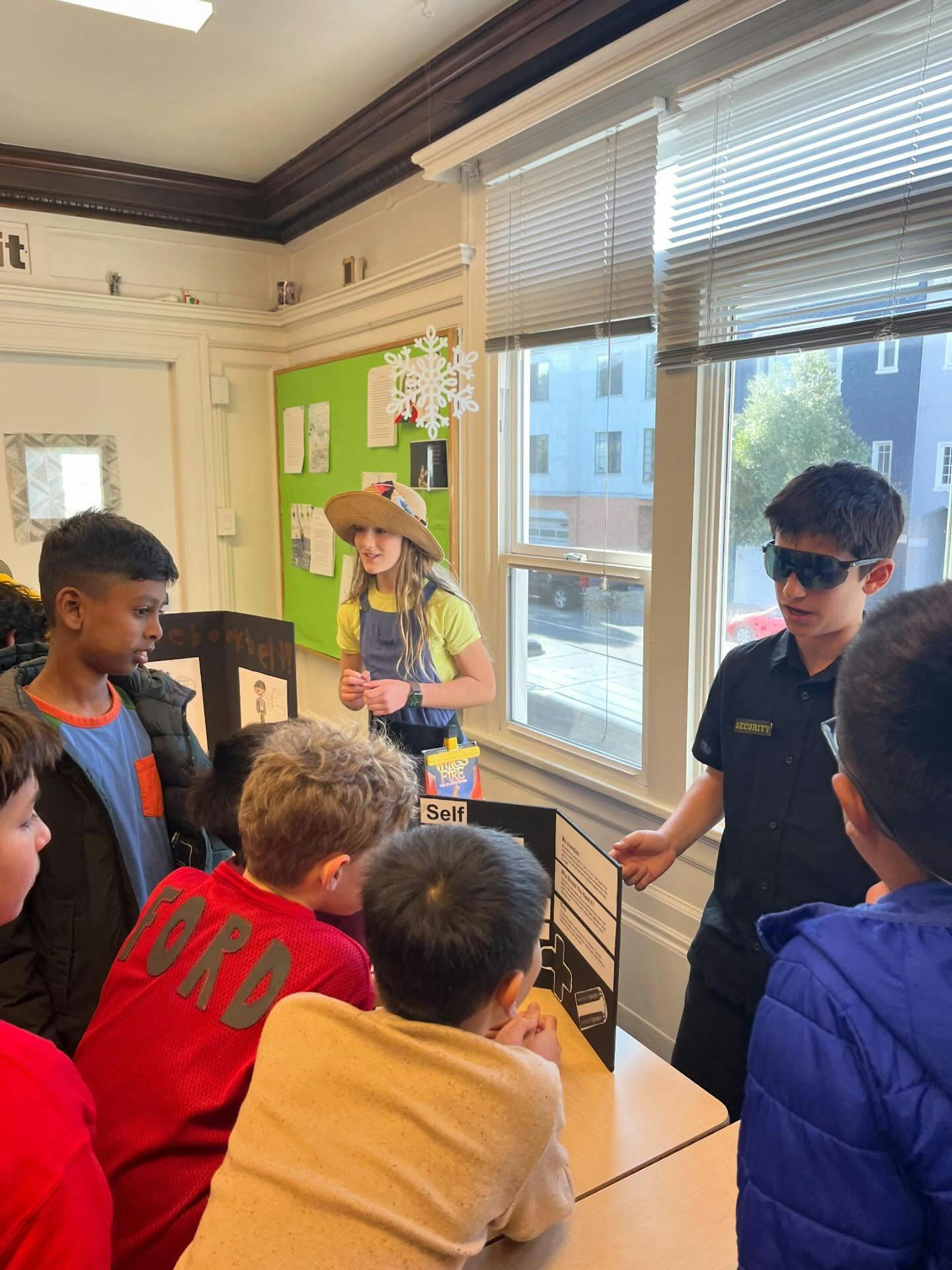 Three children presenting projects to other children in a classroom