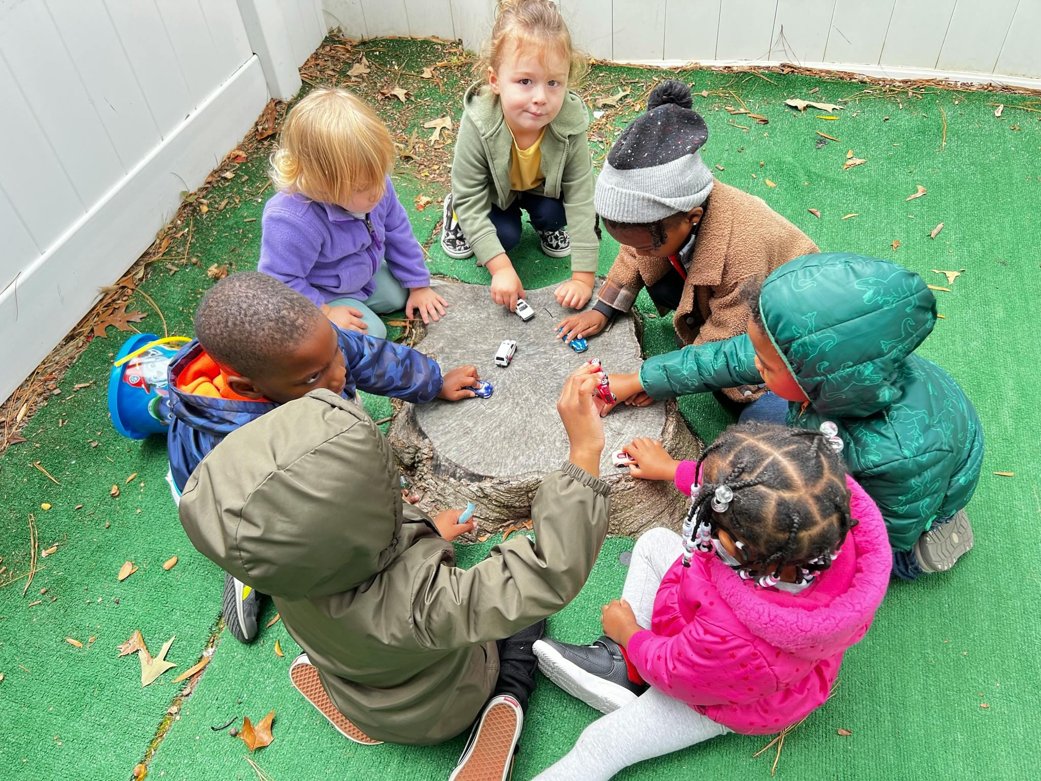 Children playing with toy cars around a tree stump