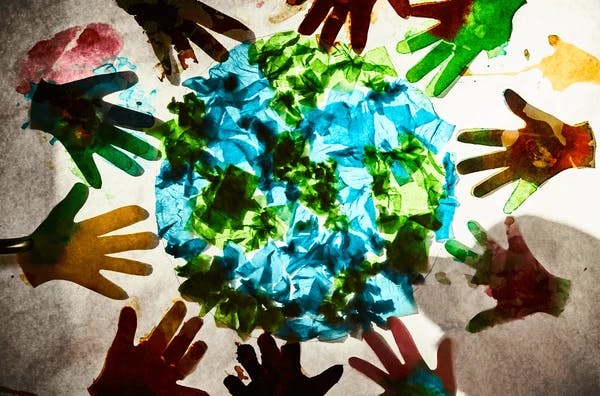 Paper cutouts of hands surrounding a blue and green paper globe