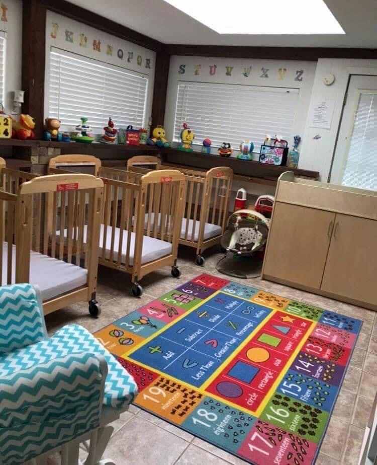Nursery room with multiple cribs, a colorful rug, and a changing table