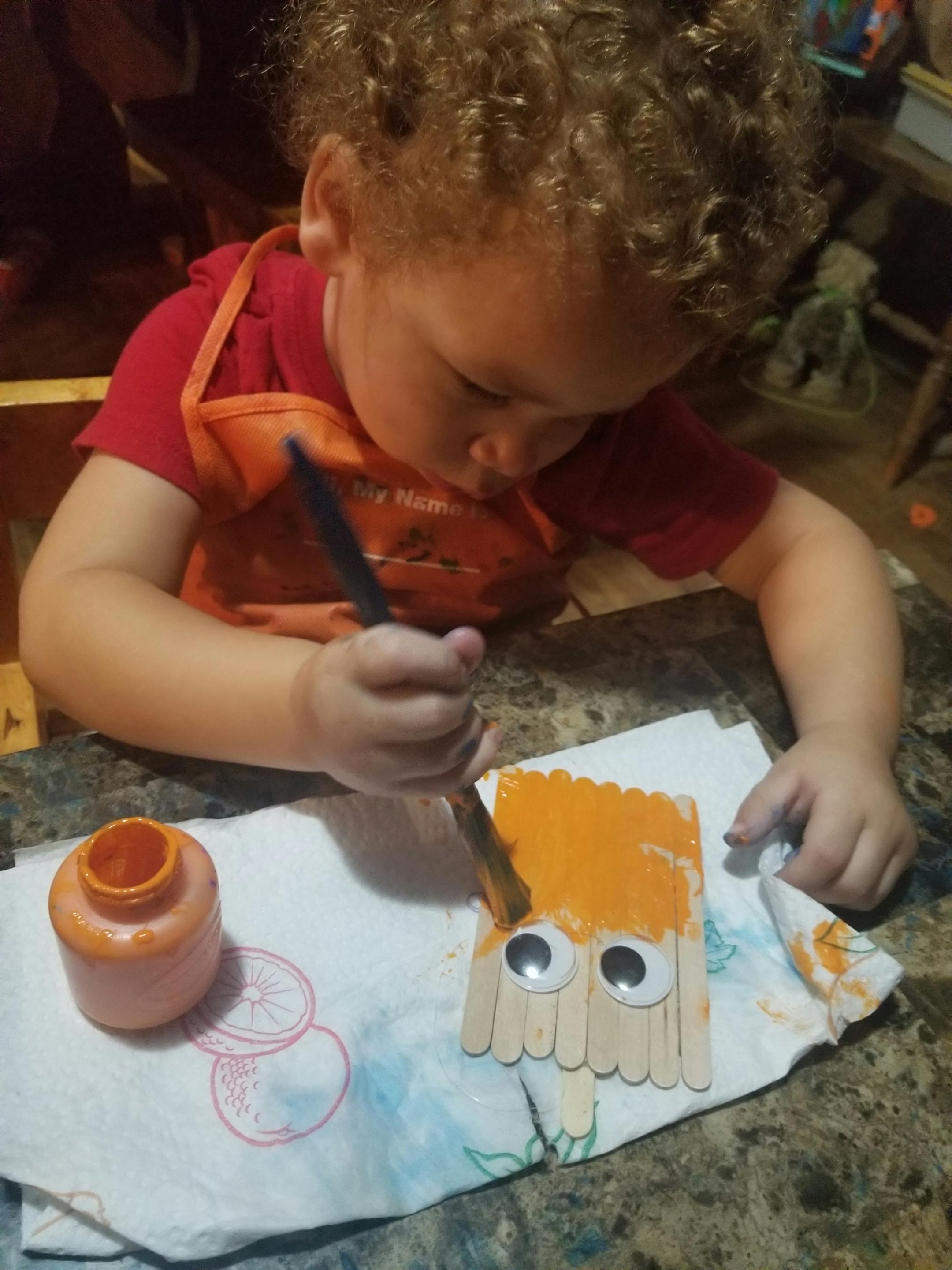 Child painting a craft stick figure with googly eyes