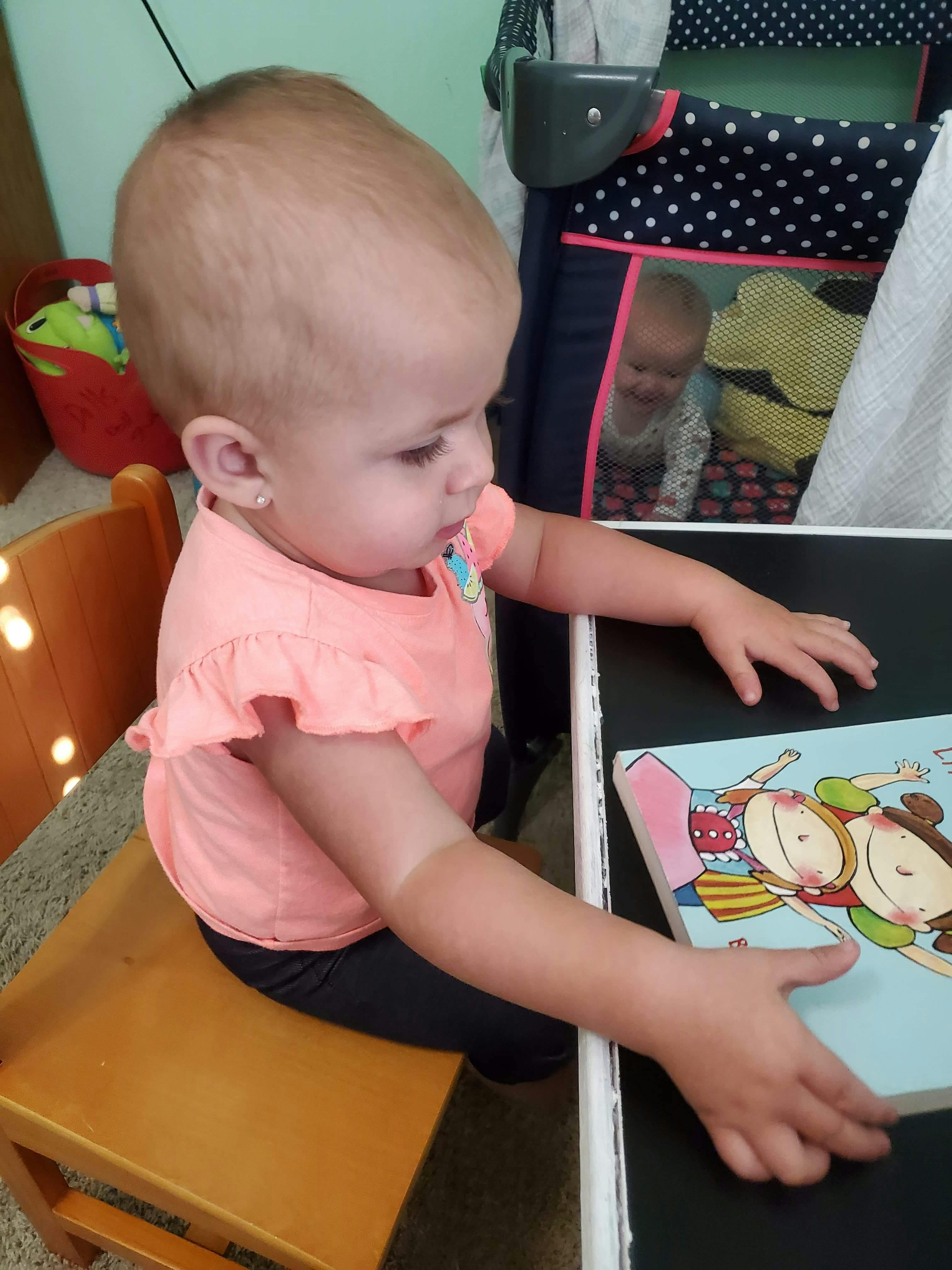 Child sitting on a chair, looking at a book on a table