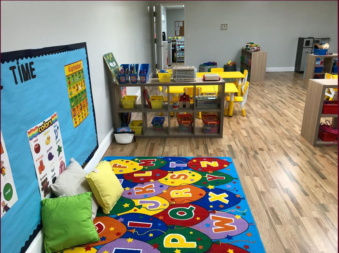 Classroom with a colorful alphabet rug, bulletin board, and yellow tables