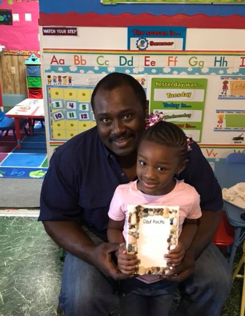 Person holding a child who is holding a decorated frame in a classroom