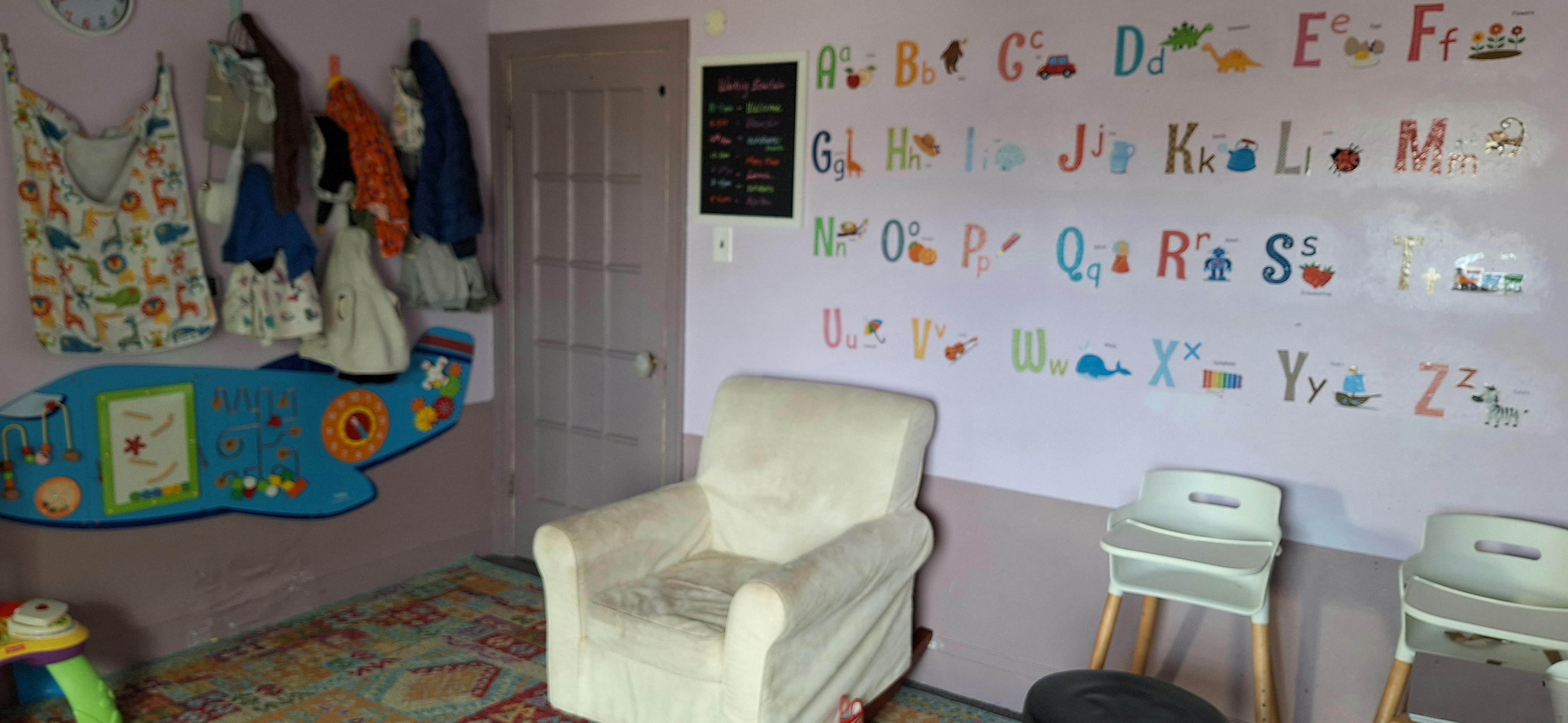Room with alphabet wall decals, a white armchair, and two high chairs