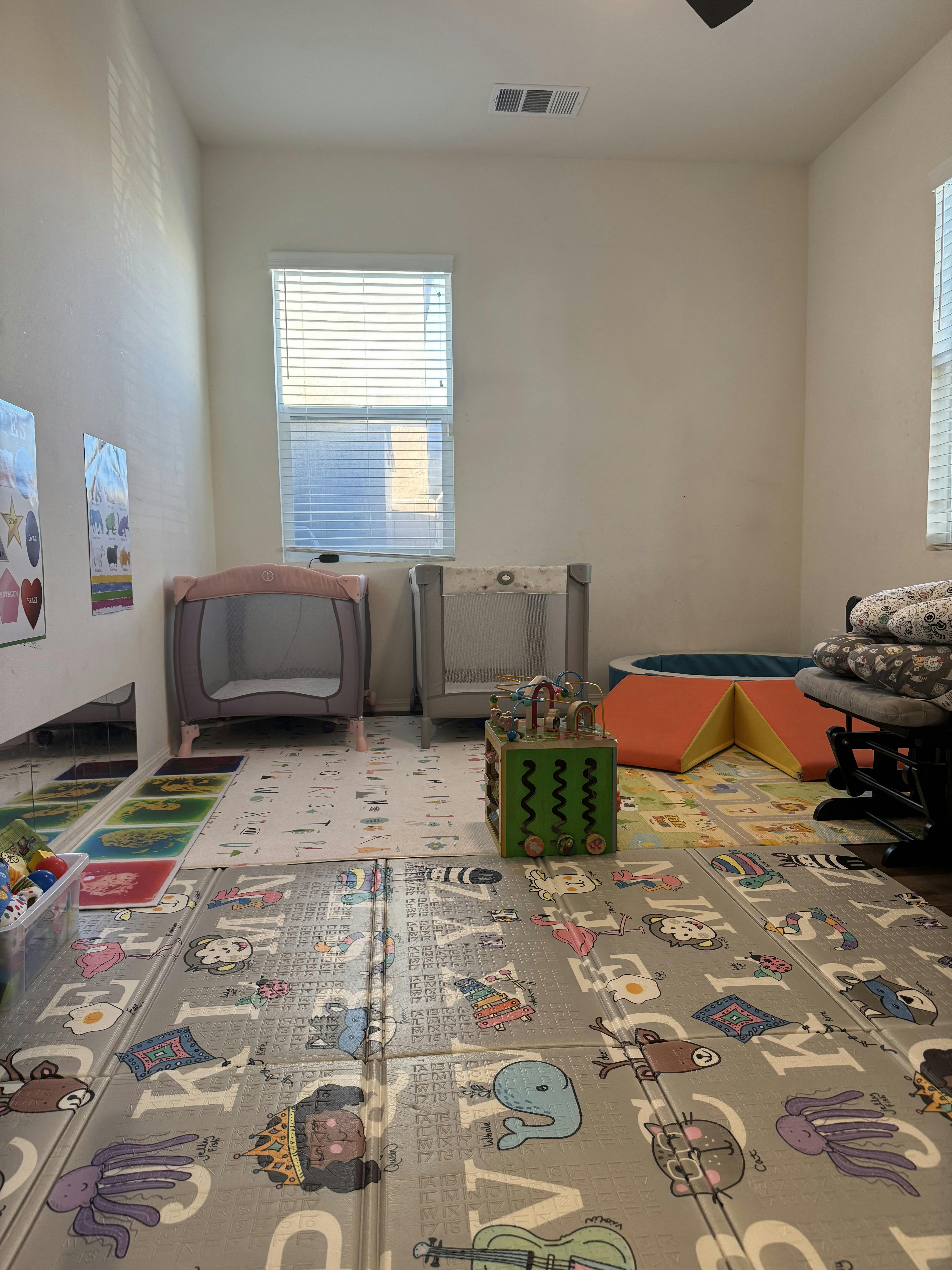 A room with two playpens, foam floor mats with animal designs, and an activity cube