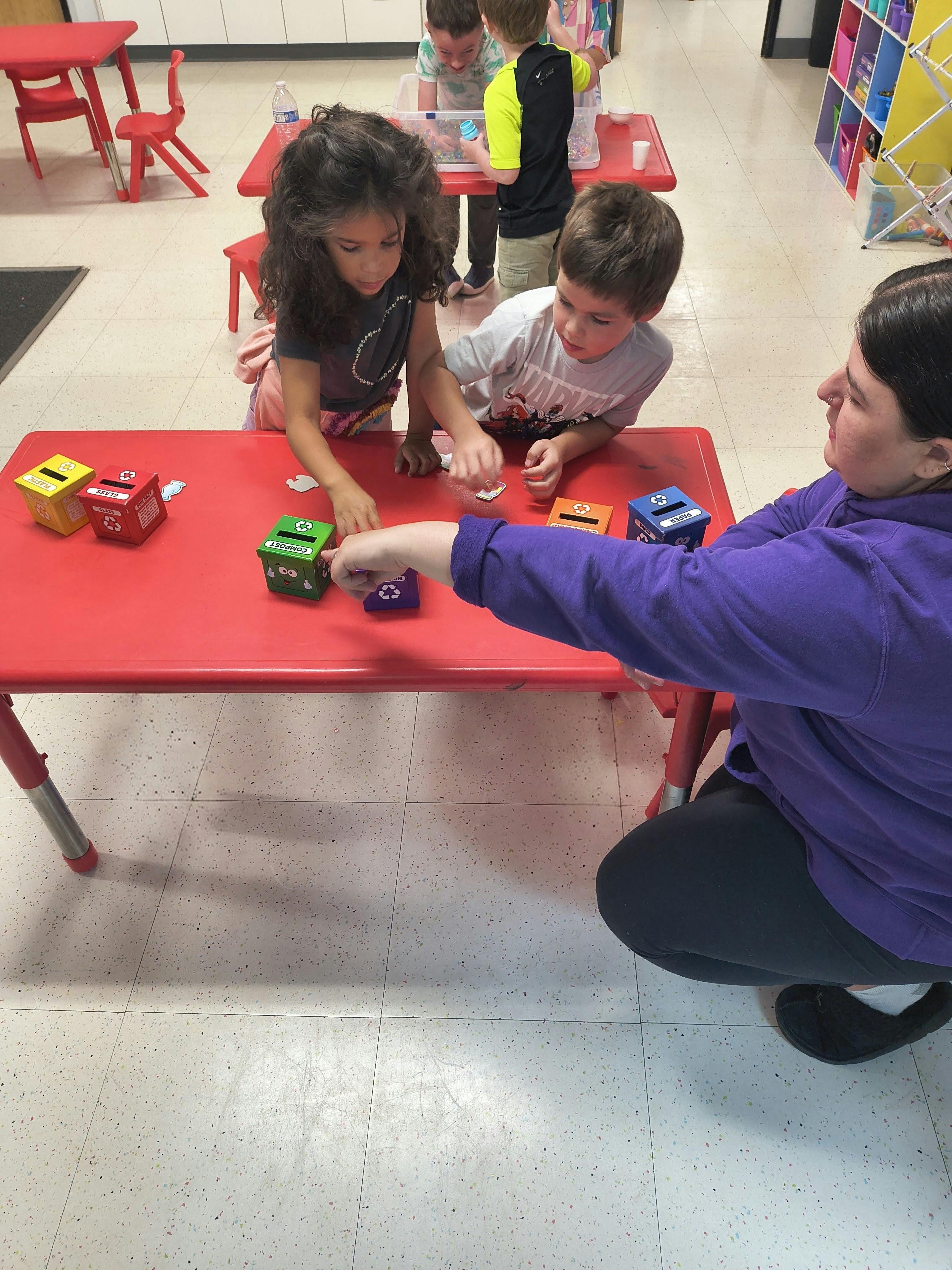 A person and children sorting small items into toy recycling bins at a table