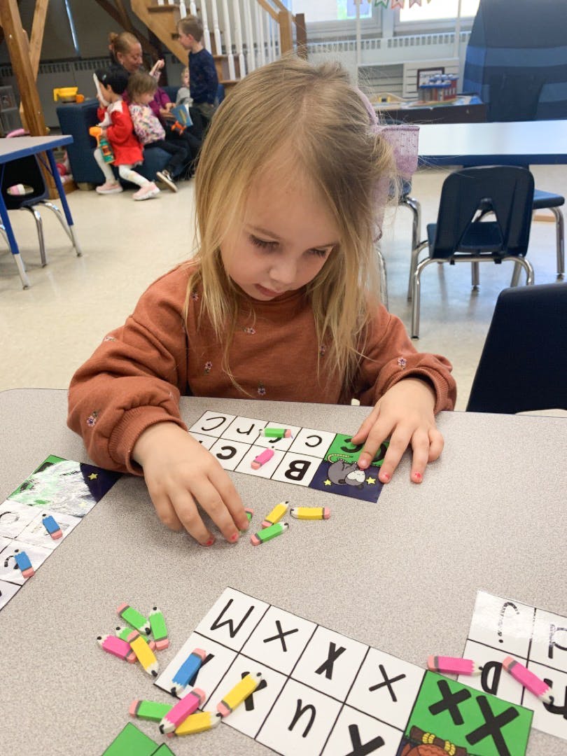 Child playing a letter matching game with small pencil erasers