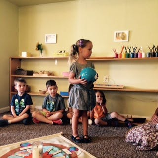 Child holding a ball while other children sit on the floor