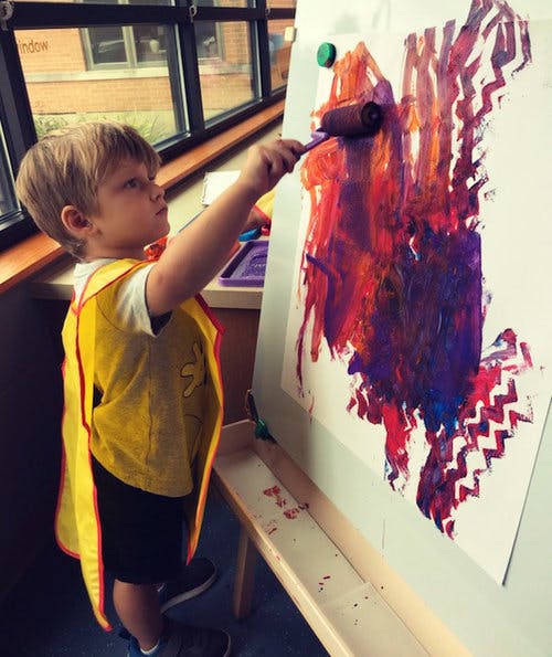 Child in yellow smock painting on an easel