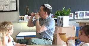 Person wearing yarmulke blowing shofar with children