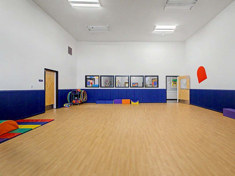 Empty children's playroom with padded blue walls, hula hoops, and colorful mats