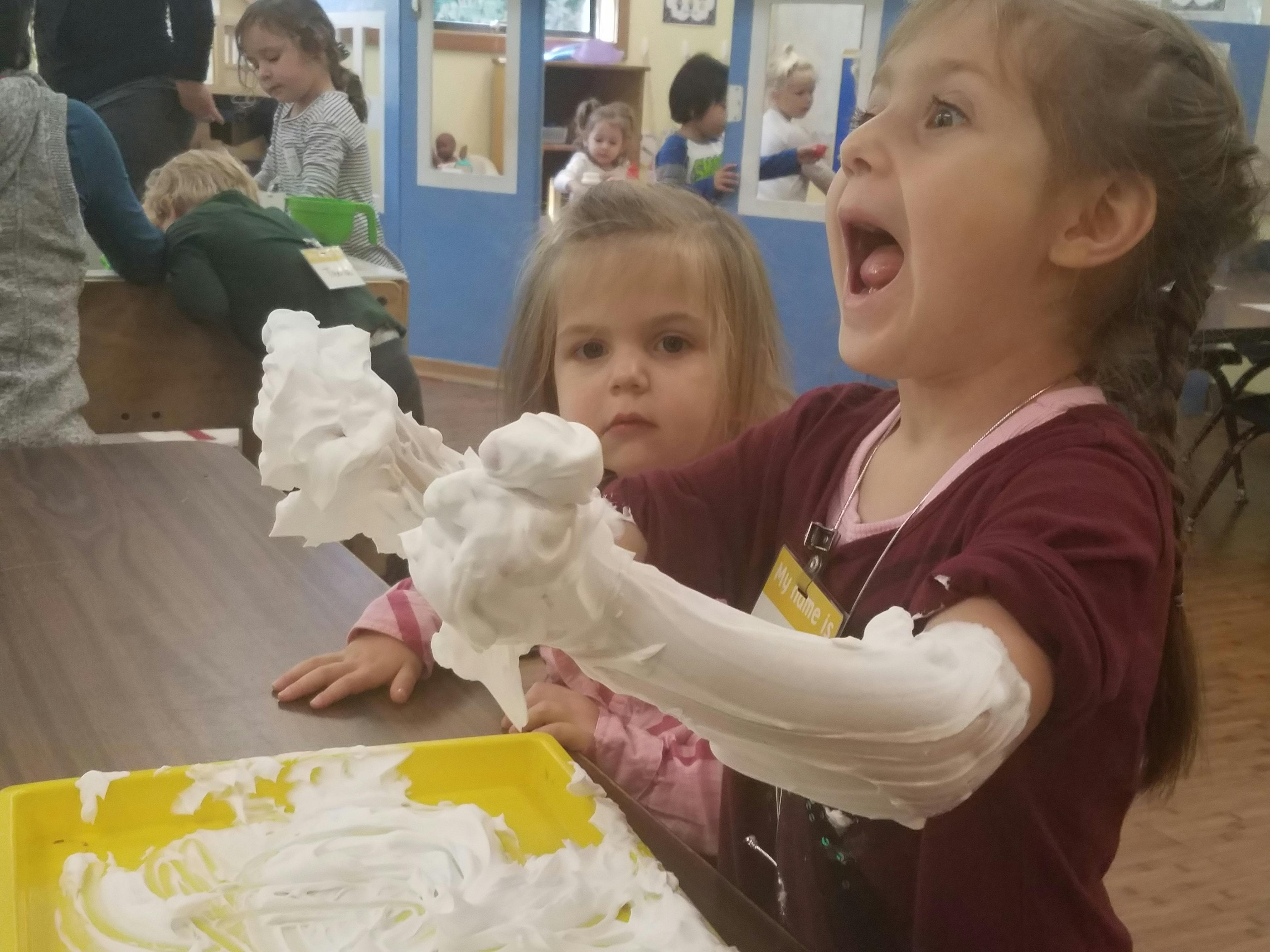 Child with arms covered in white foam, another child in background