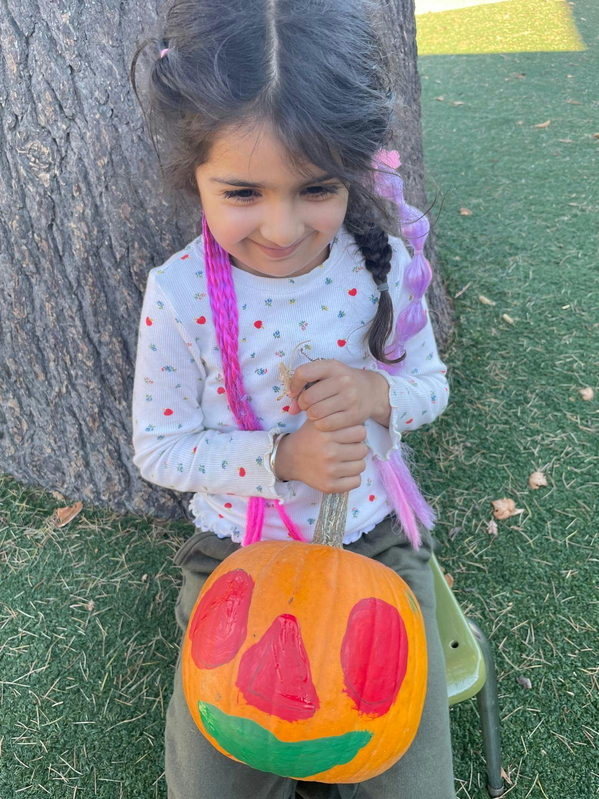 Child holding a painted pumpkin while sitting outdoors