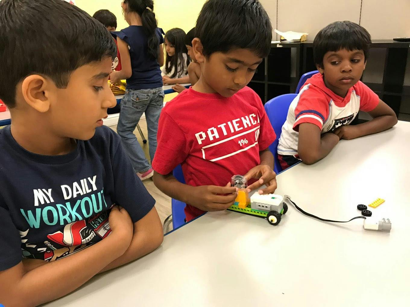 Three children at a table, one child assembling a small toy car