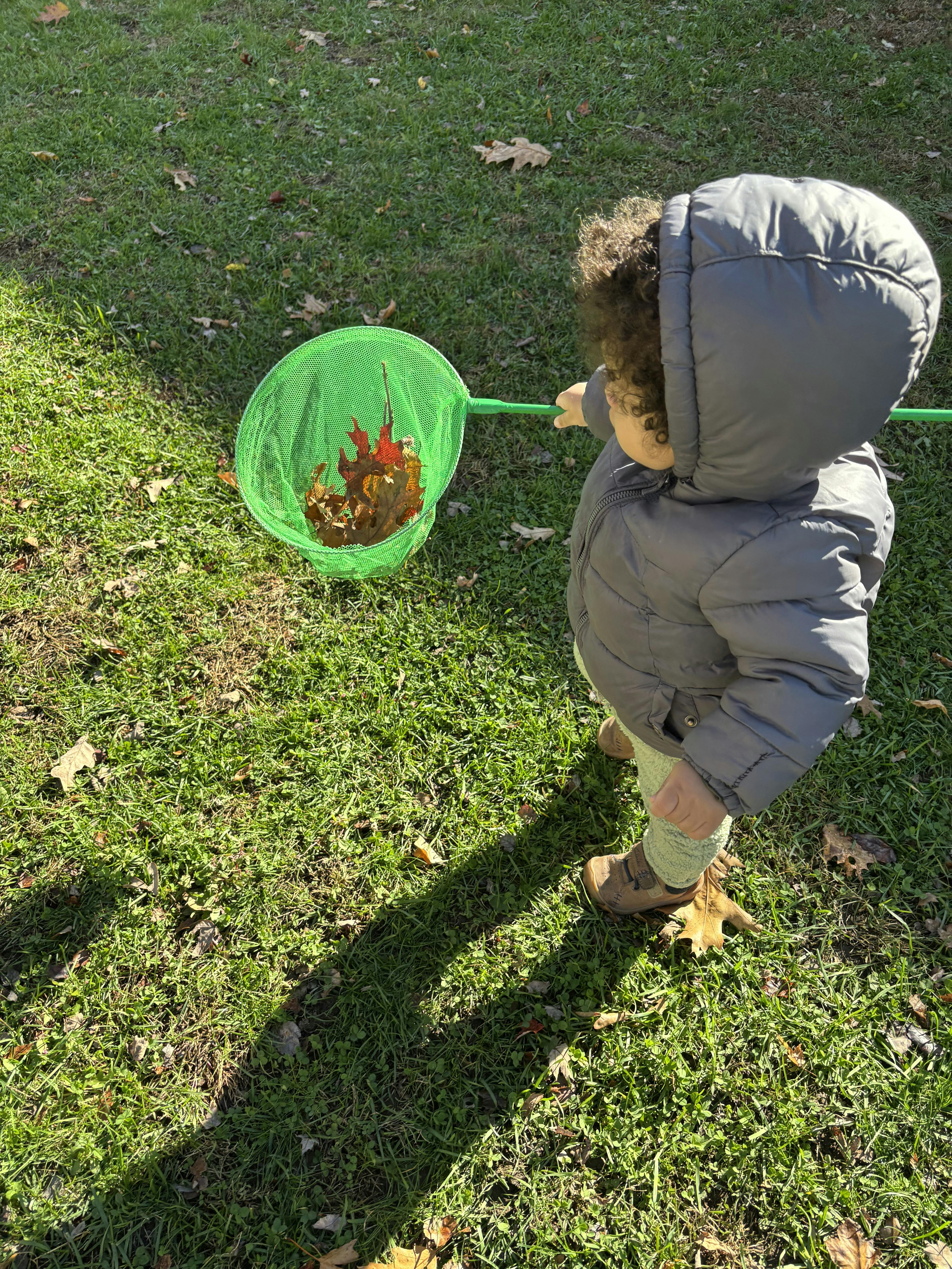 Child in a hooded coat holding a green net with leaves in it