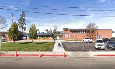 School building with a grassy area and a parking lot with cars