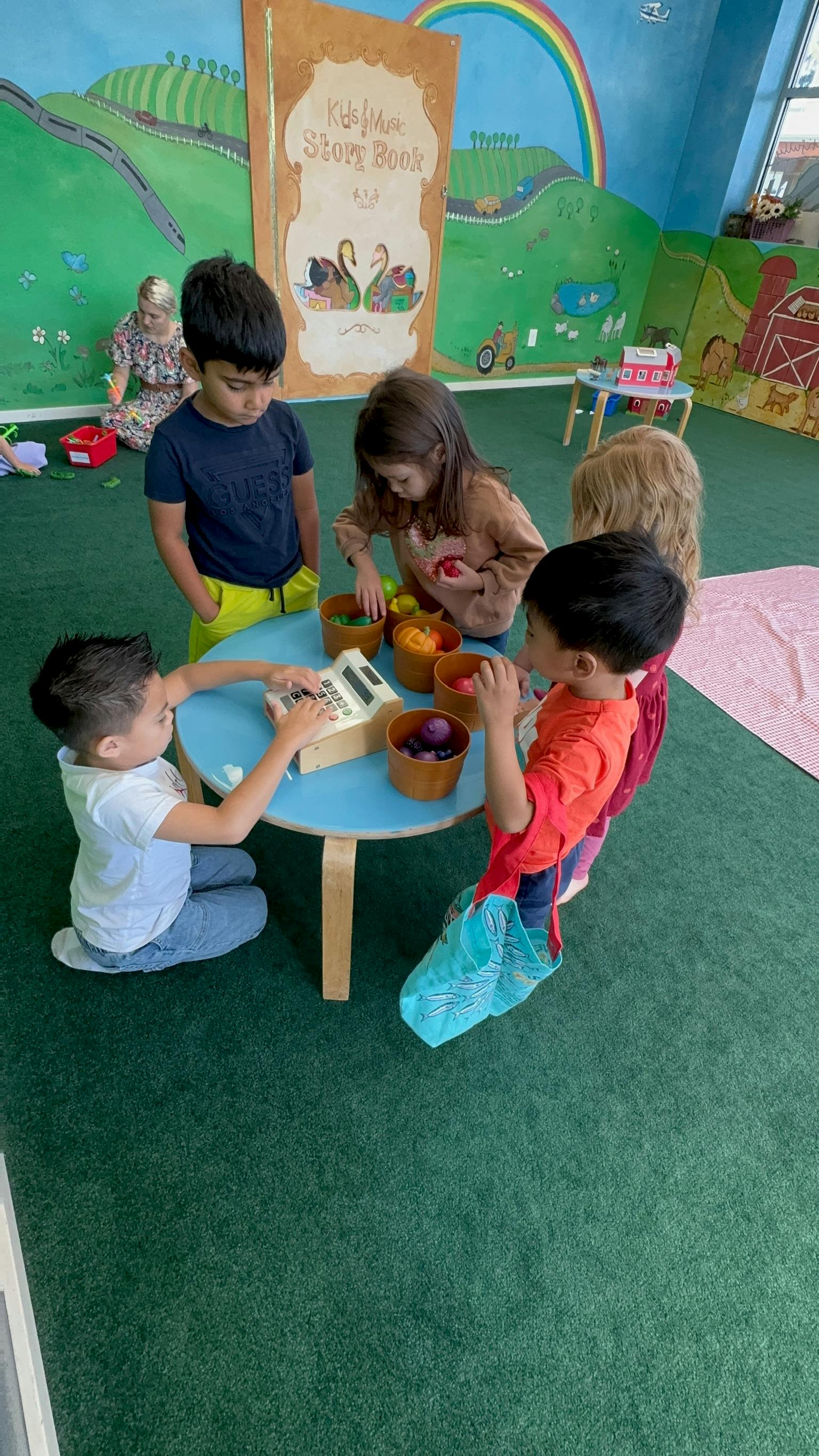Children playing with a toy cash register and pretend food at a small table