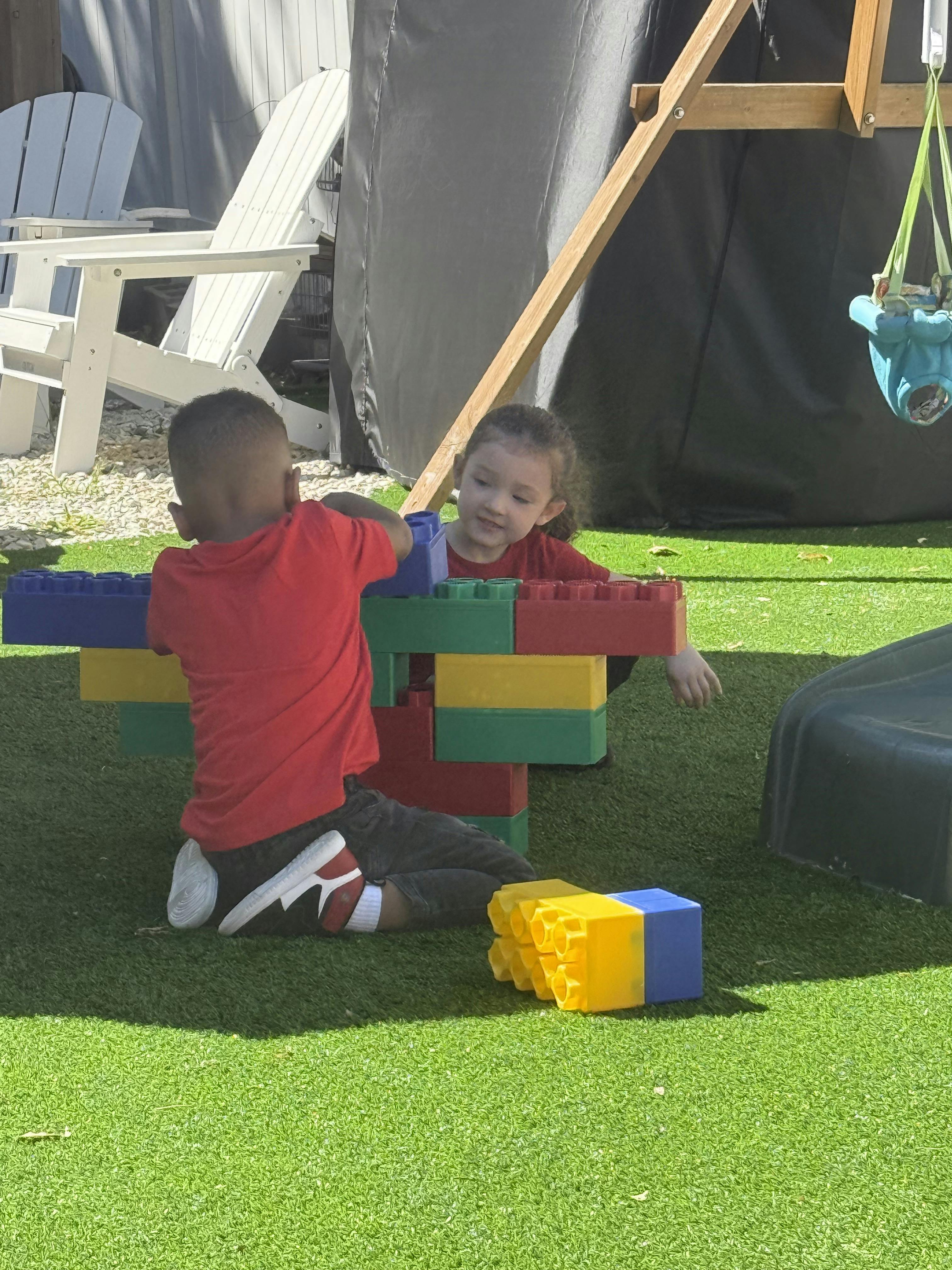 Two children playing with large colorful building blocks on grass