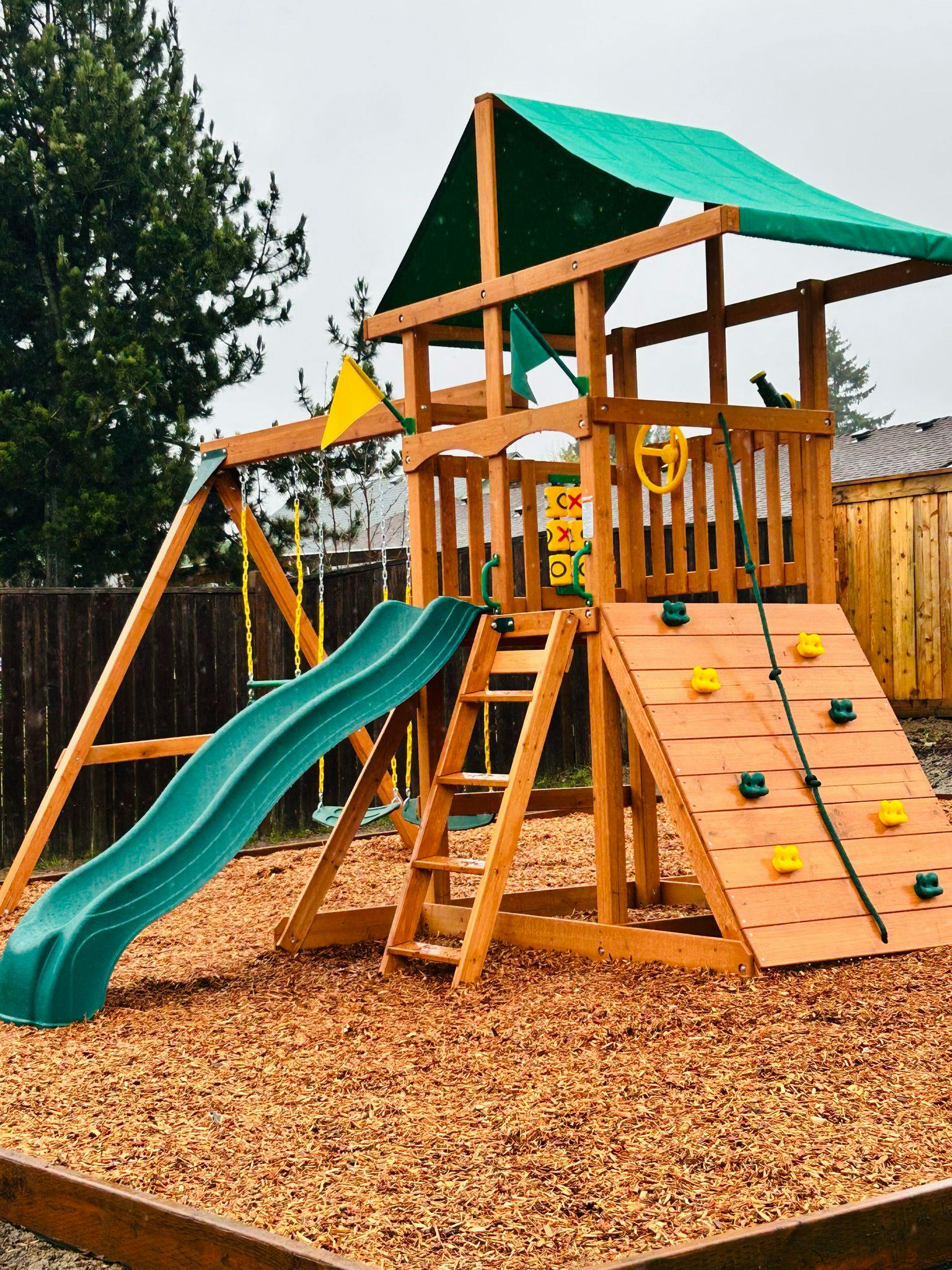 Wooden playground set with slide, swings, and climbing wall