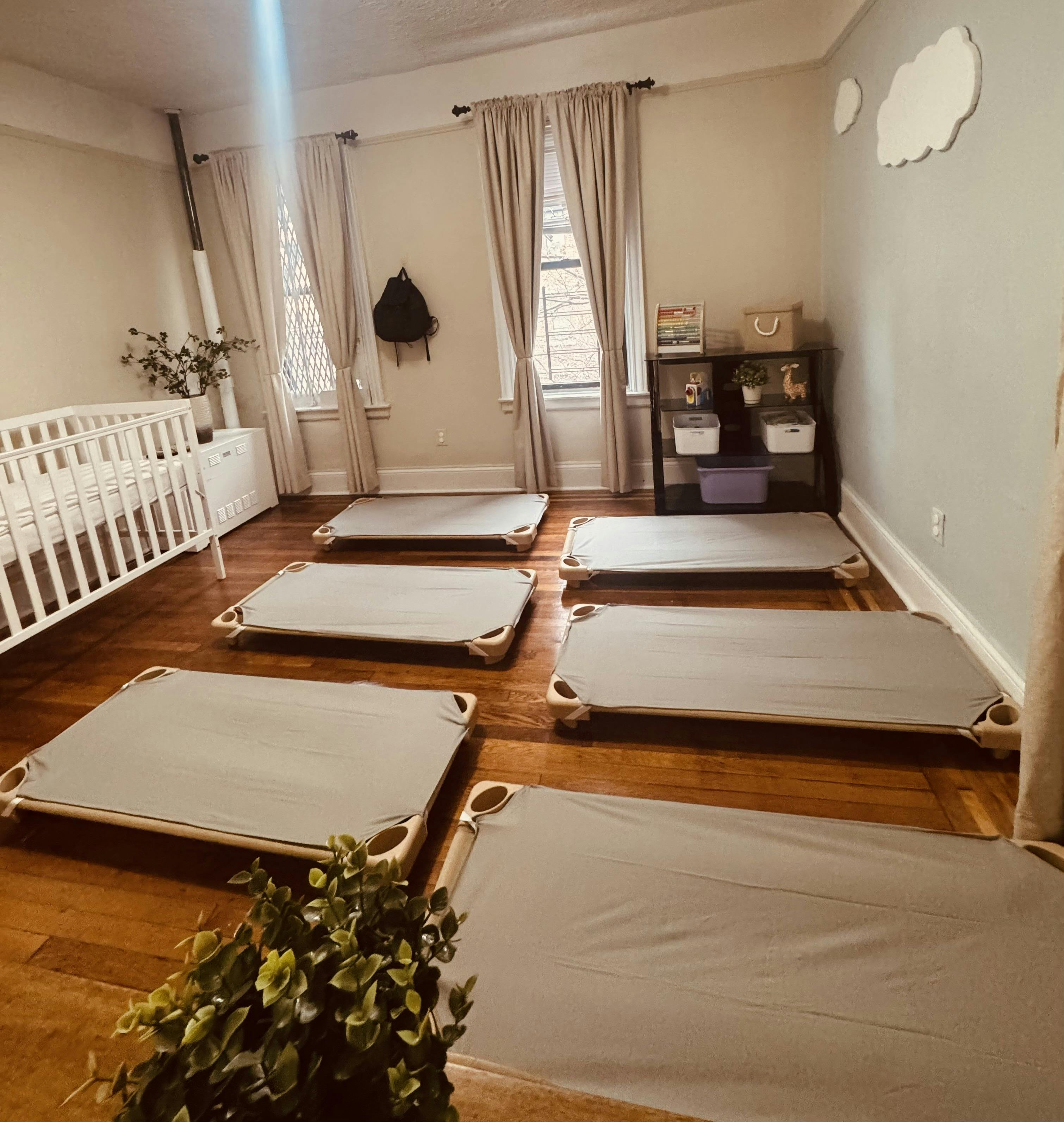 multiple toddler cots on a hardwood floor next to a white crib