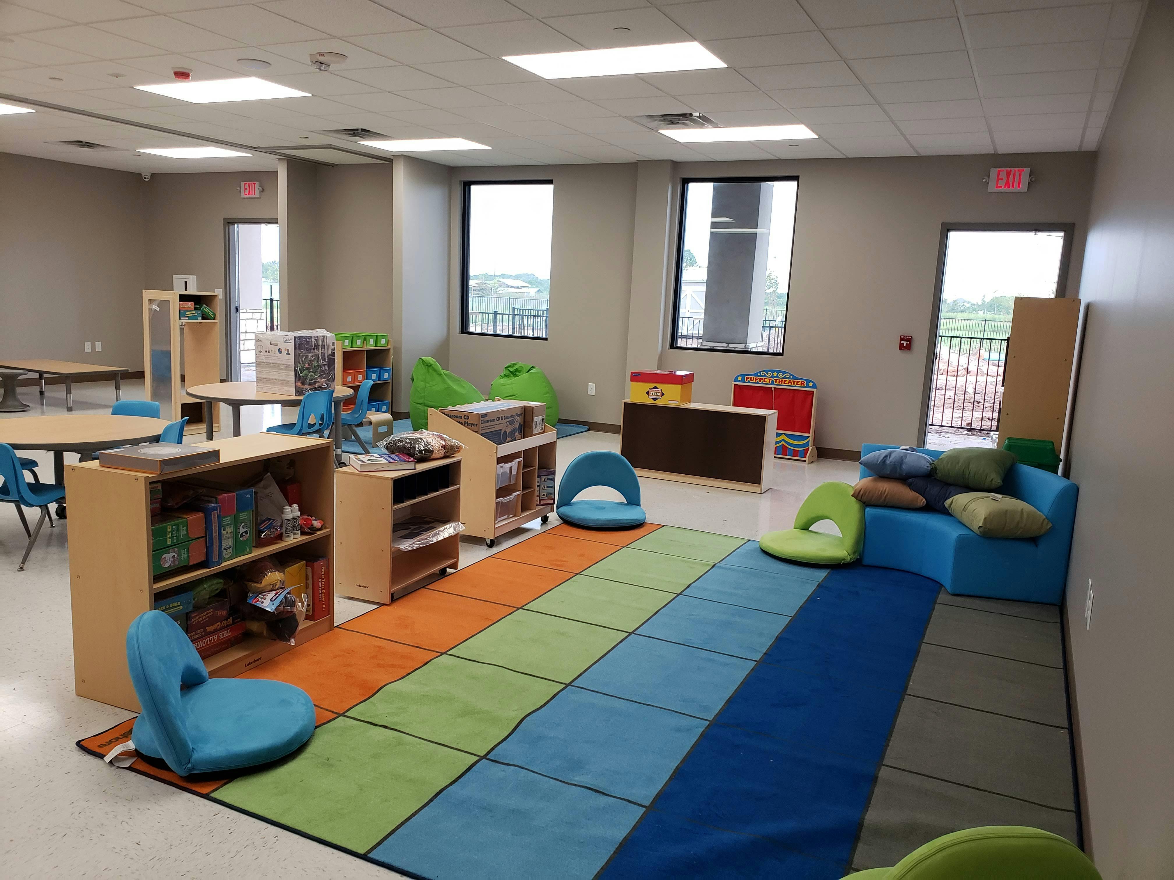 Classroom with colorful rug, small chairs, tables, and bookshelves