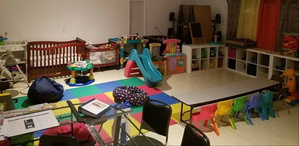 Playroom with cribs, colorful floor mats, small slide, and children's table and chairs