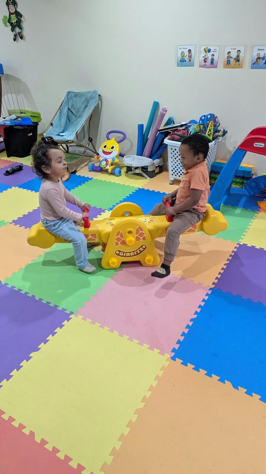 Two children playing on a giraffe seesaw on a colorful foam play mat