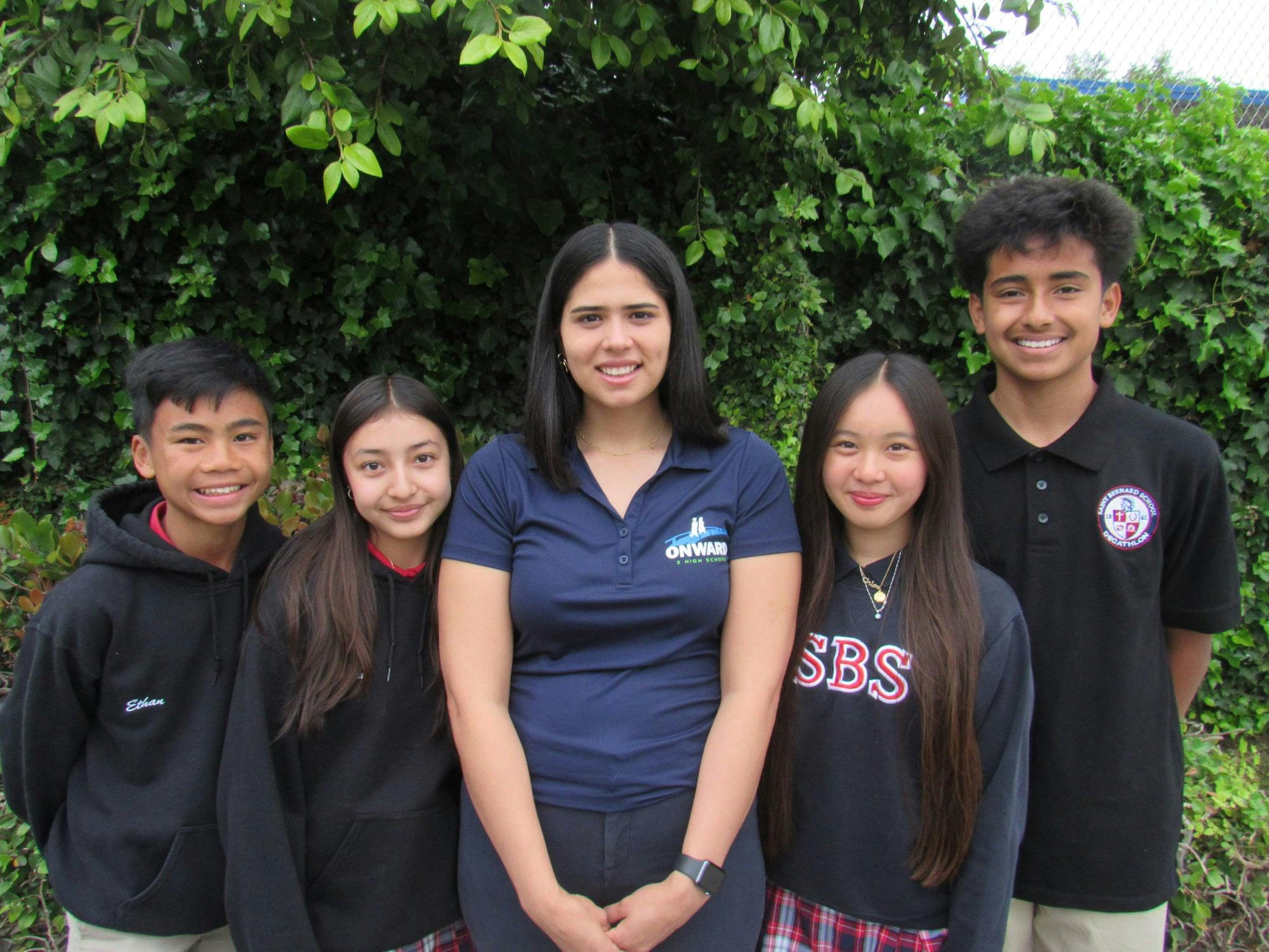 Five people standing outside in front of green foliage
