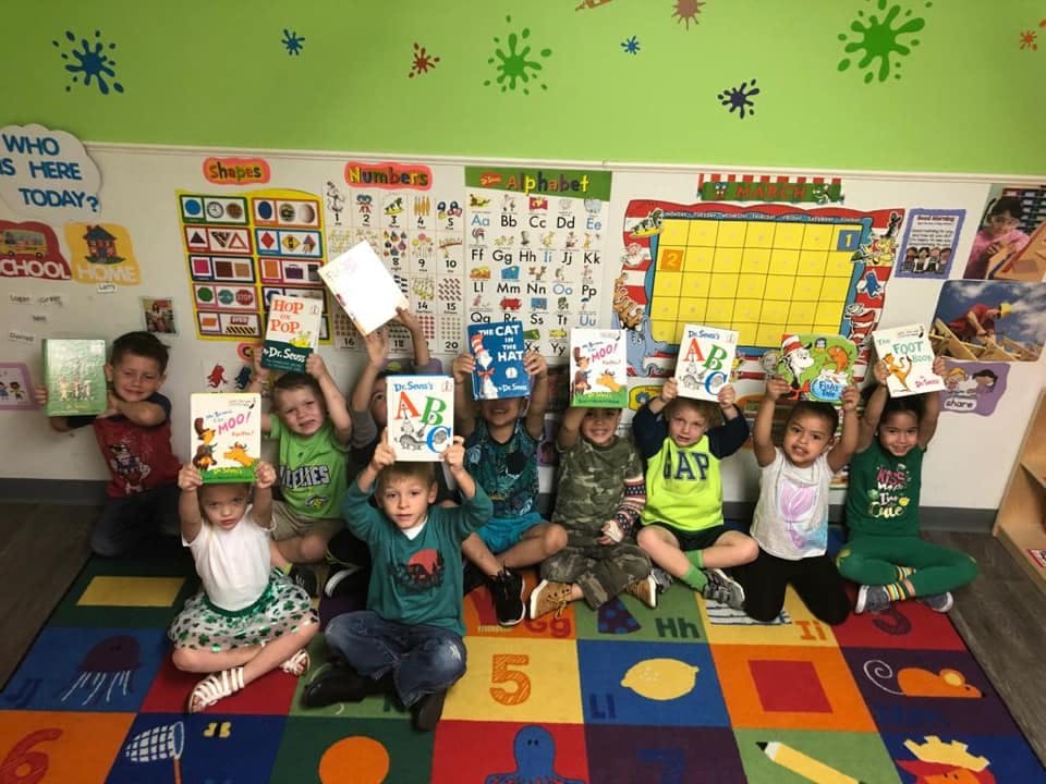 Children sitting on a rug holding books above their heads in a classroom