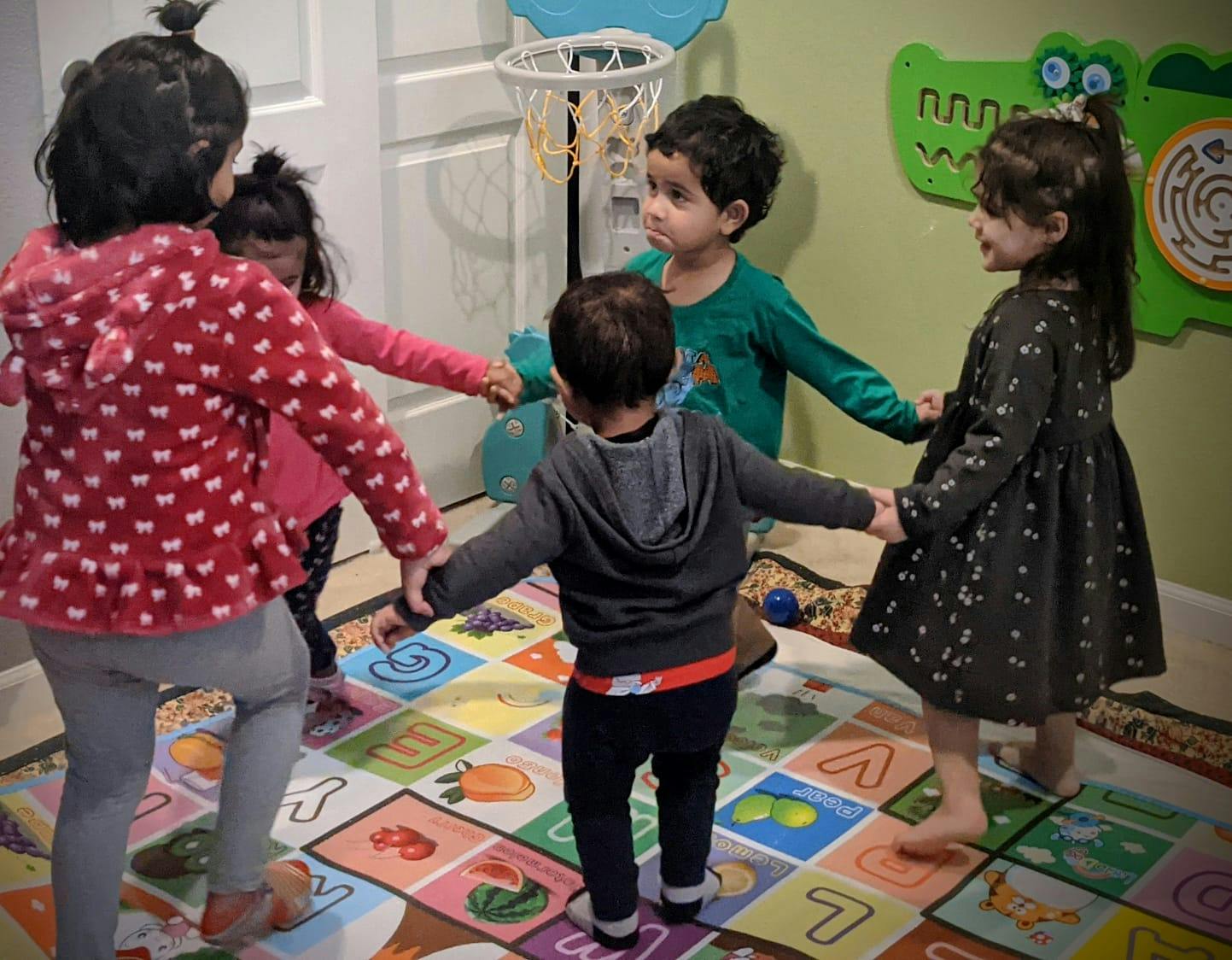 Five children holding hands in a circle on a colorful rug