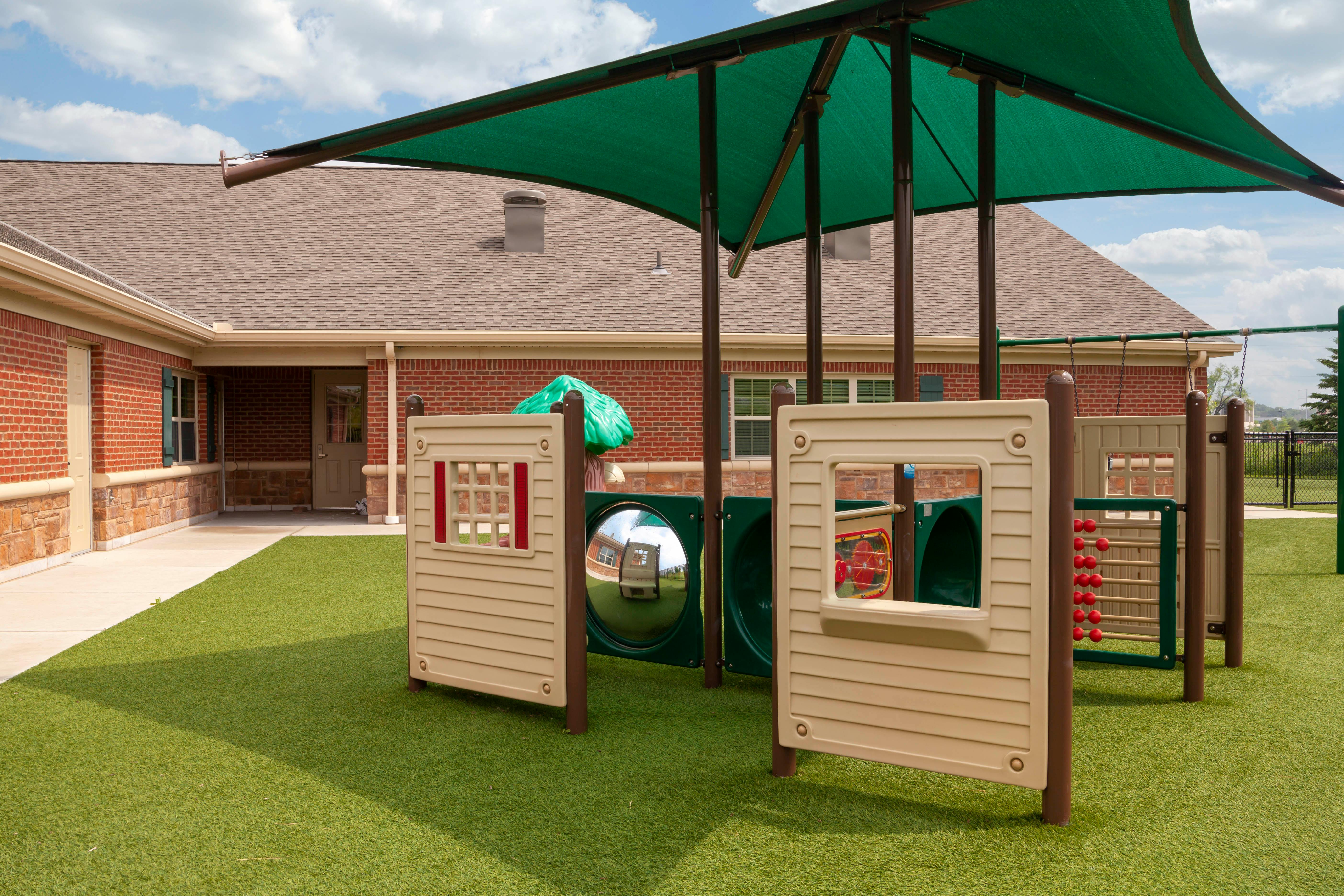 A children's playground with green turf and play structures under a large shade