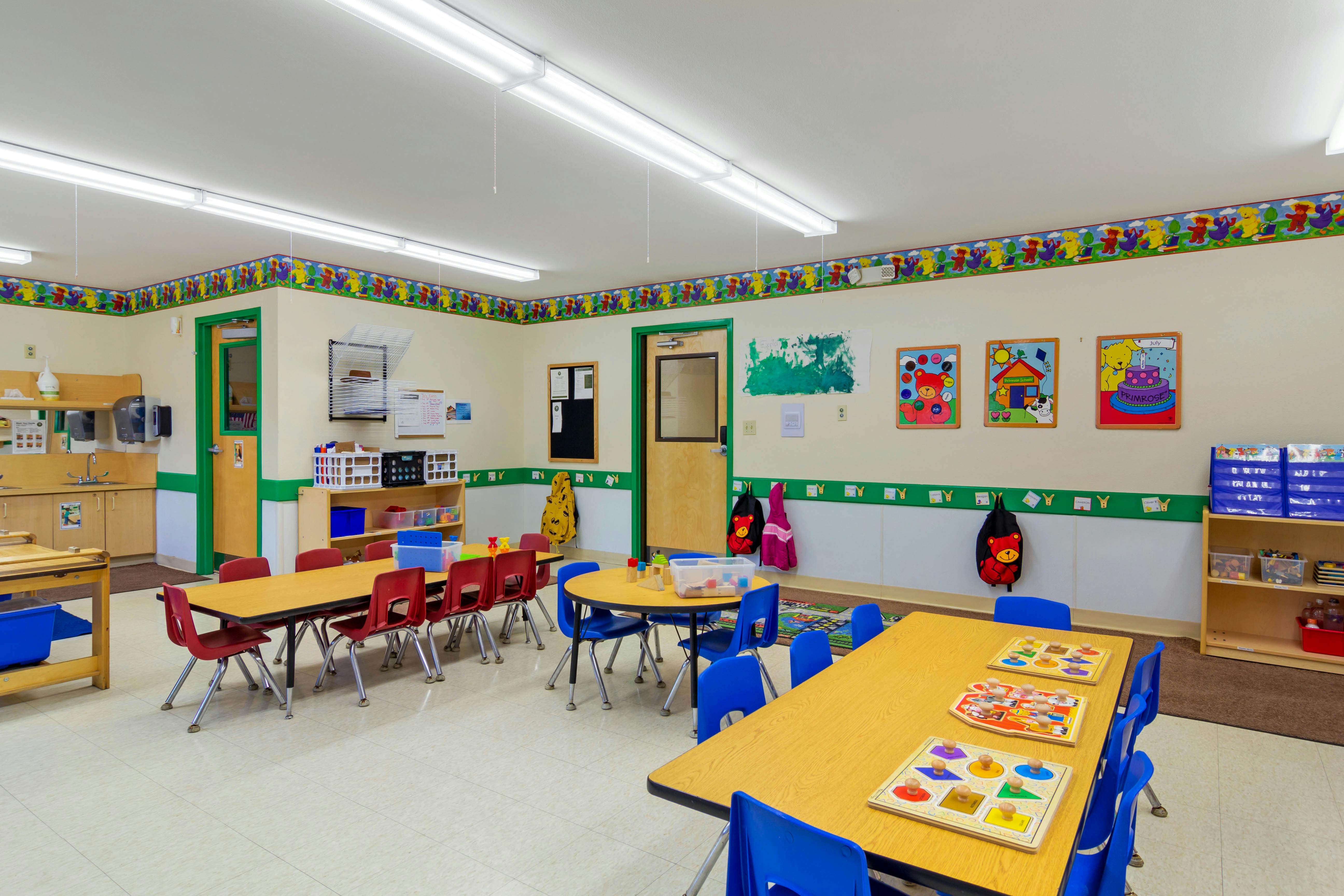 Empty colorful preschool classroom with tables, chairs, and learning materials