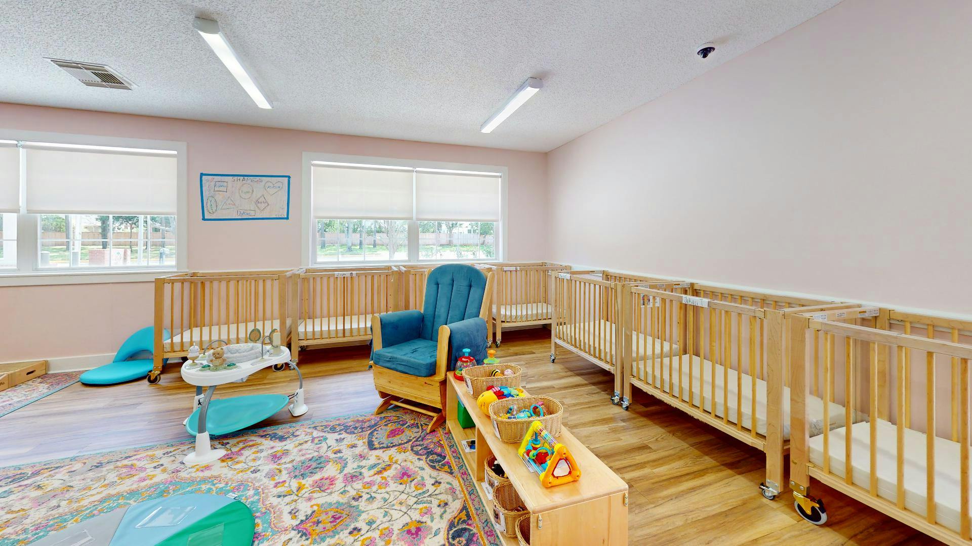 Room with multiple cribs, a rocking chair, and toys