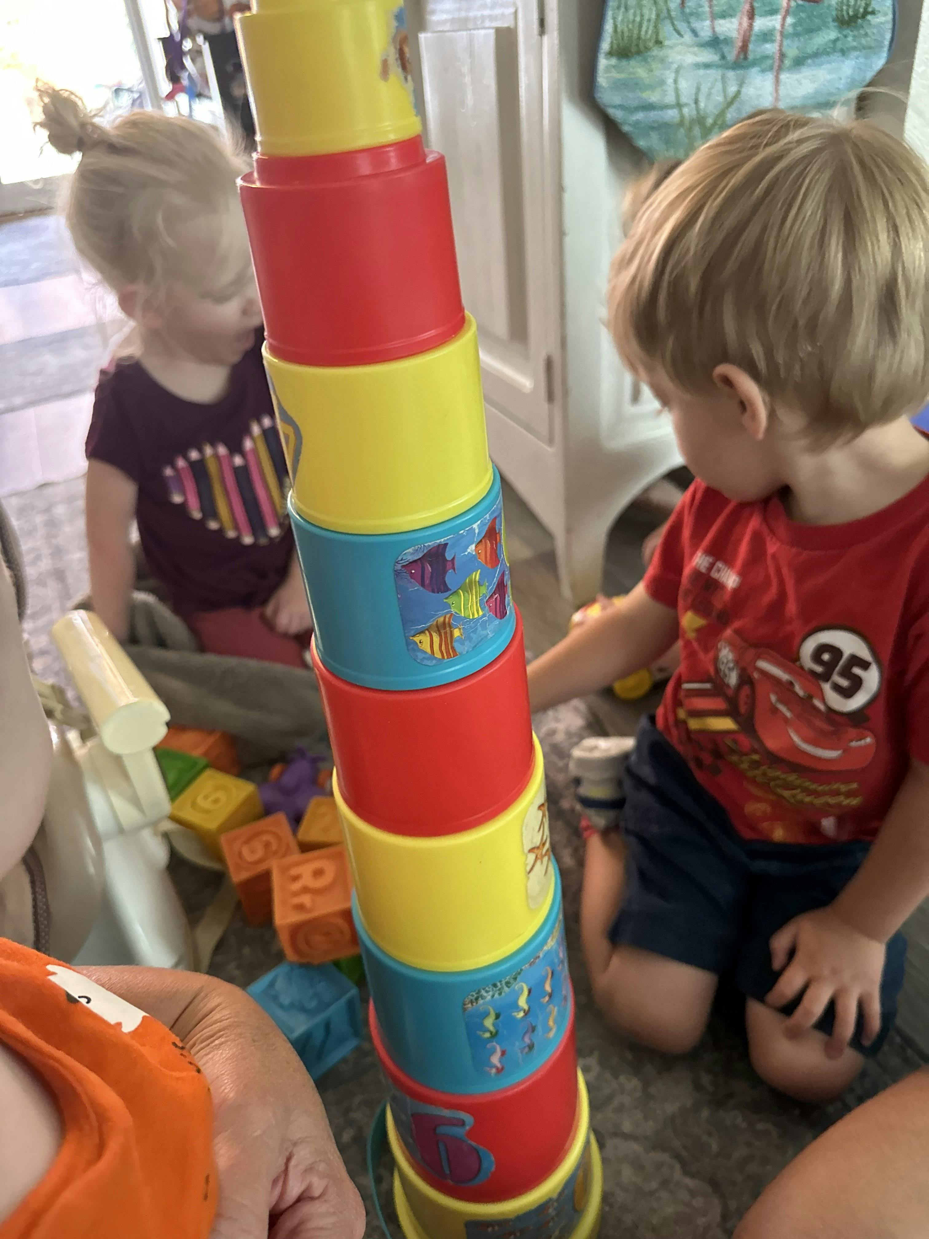 Children playing with a tall stack of colorful nesting cups